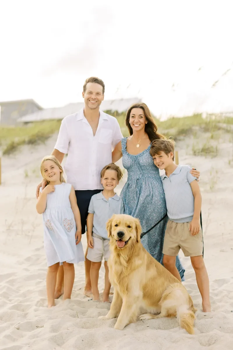 The Oates family and their dog on the beach, smiling at the camera.