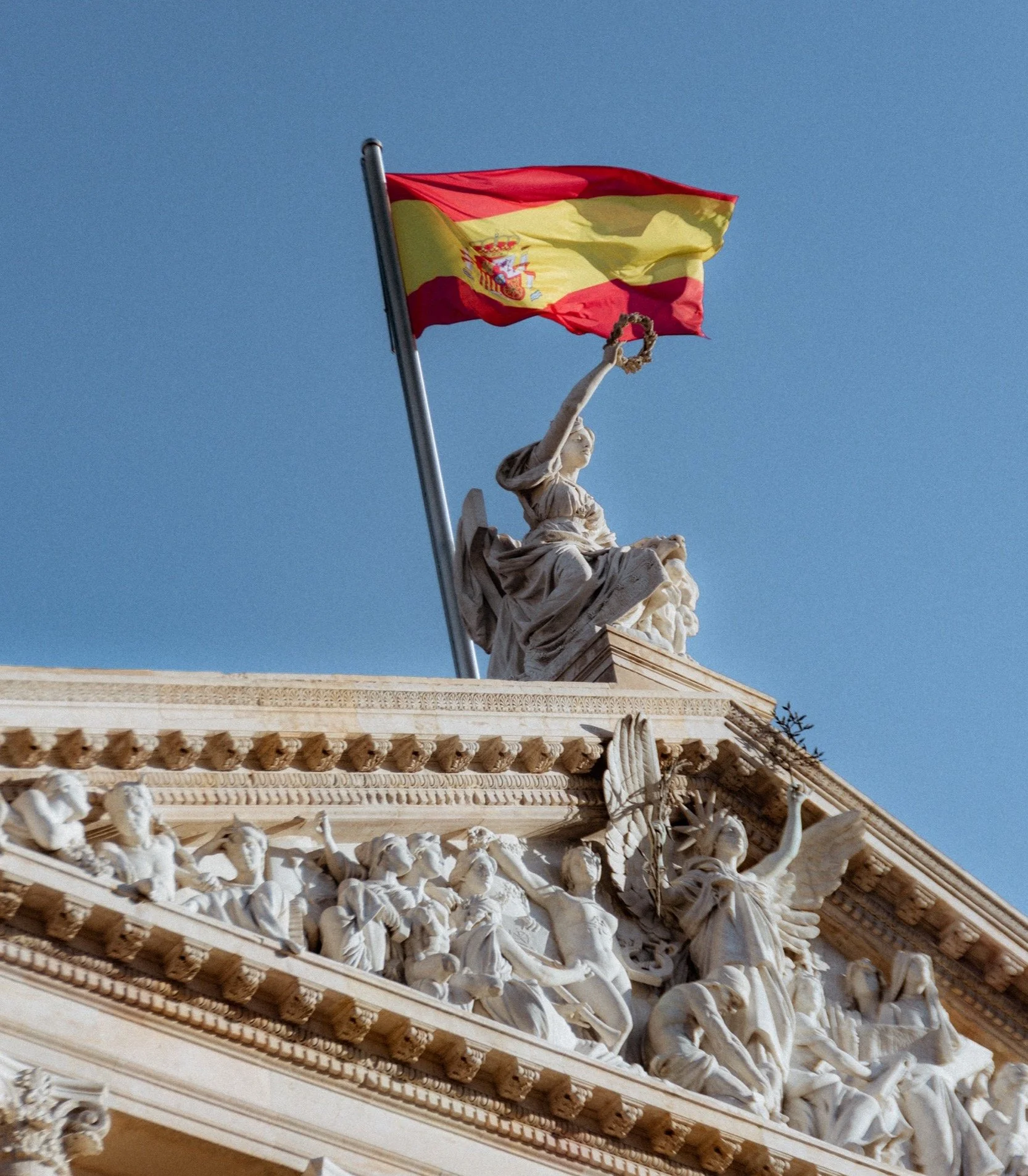 Top of building in Madrid, Spain with Spanish flag waving against the sky. Sourced from the Rosewood in Madrid