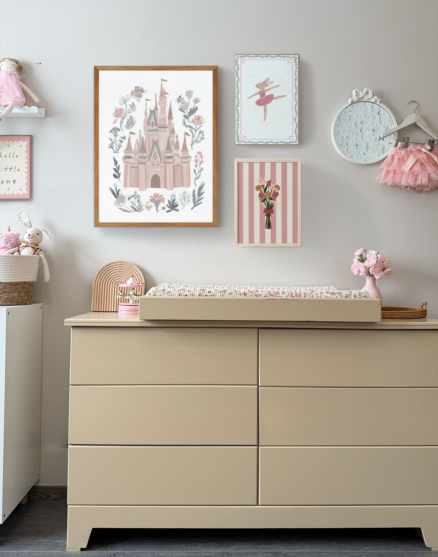 Habitación infantil con armario beige, decoraciones en tonos rosados y blancas, cuadros de dibujos de cuentos de hadas y bailarinas, y detalles de juguetes y flores.