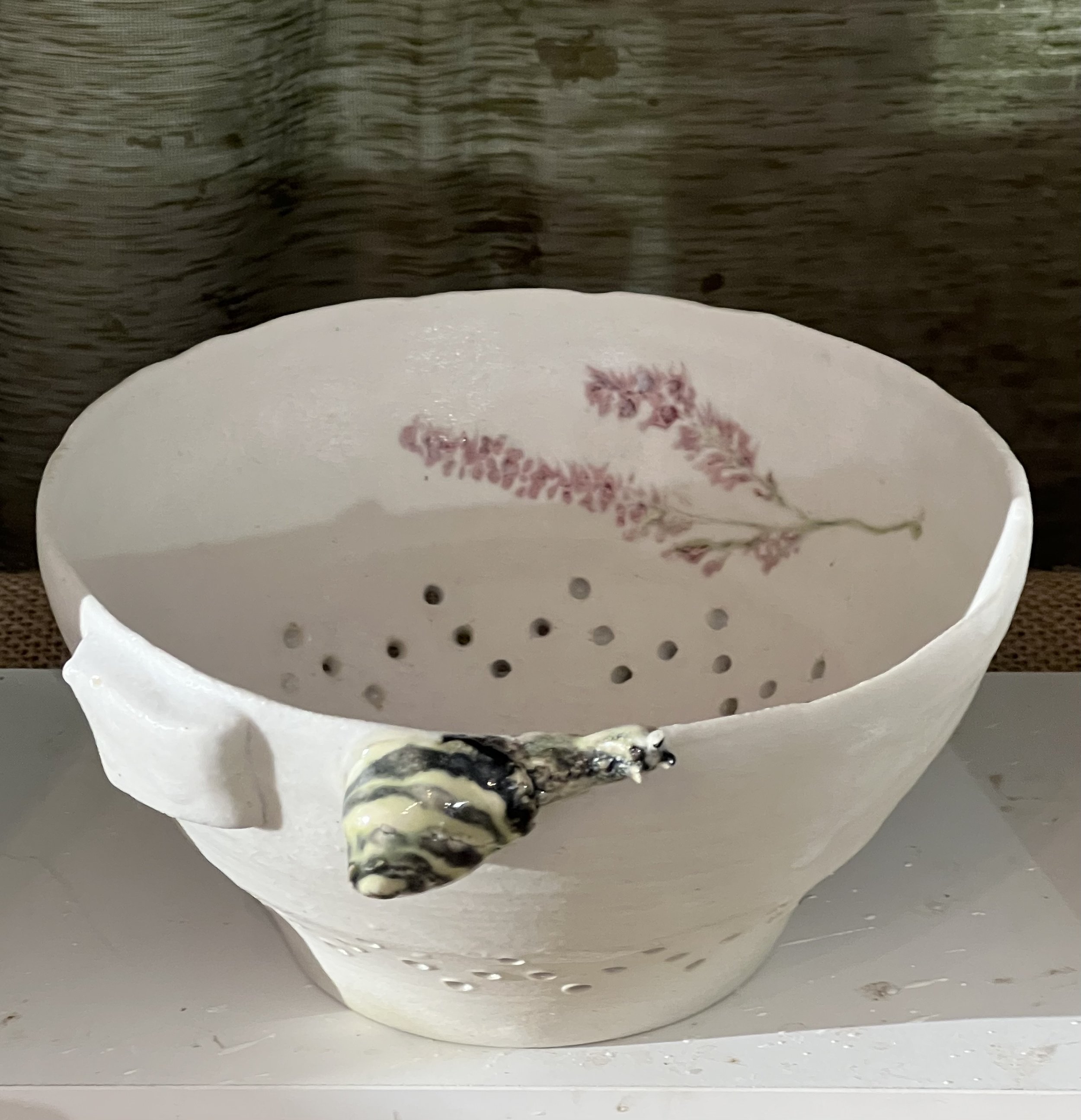 Une tasse blanche avec une décoration florale rouge, vue de dessus, contenant un liquide noir avec des morceaux de crème ou de mousse, posée sur une surface grise.