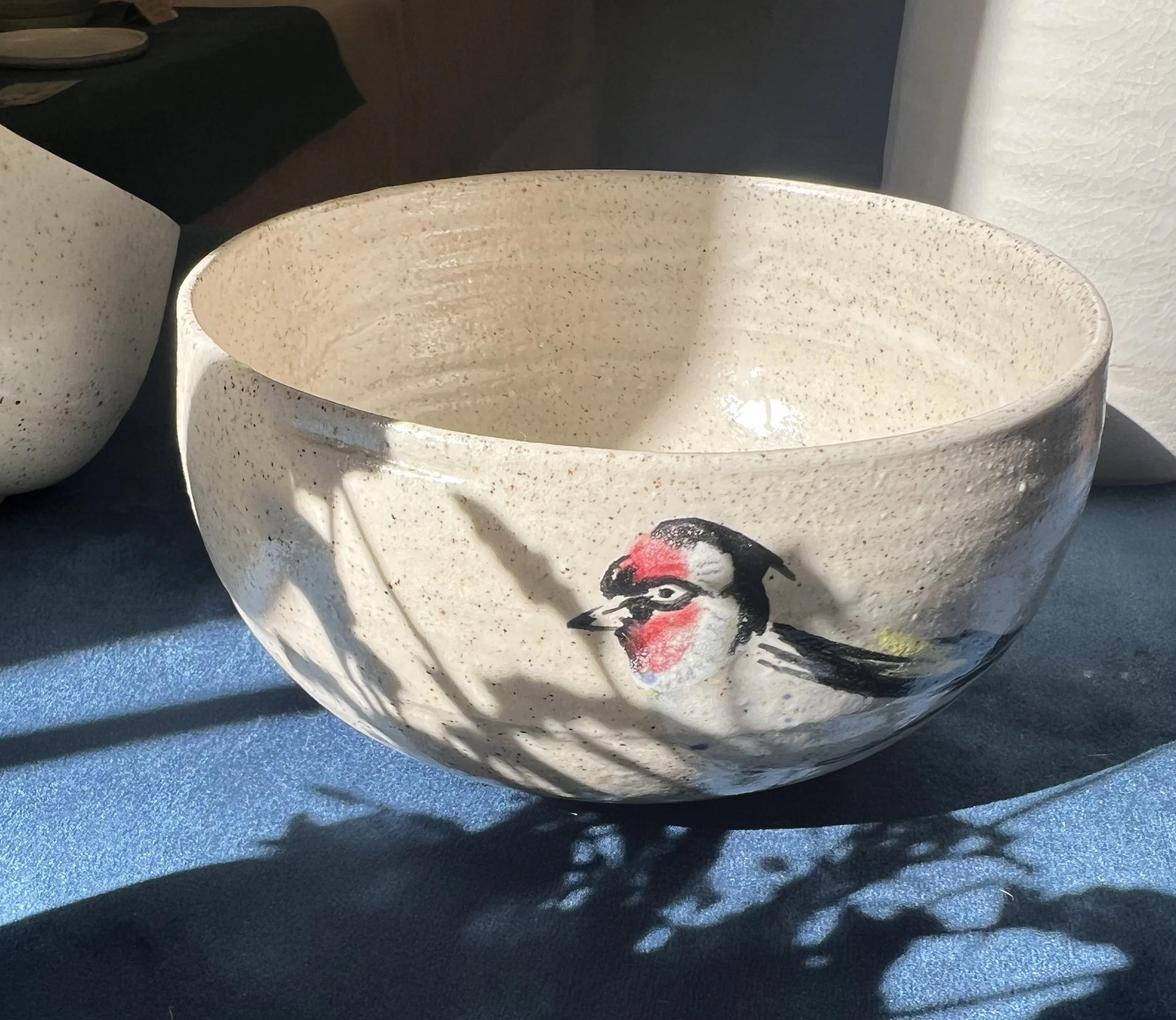 Une assiette en céramique beige avec des points noirs et un motif de pieuvre, posée sur une surface noire avec un fond blanc et une autre assiette visible en arrière-plan.