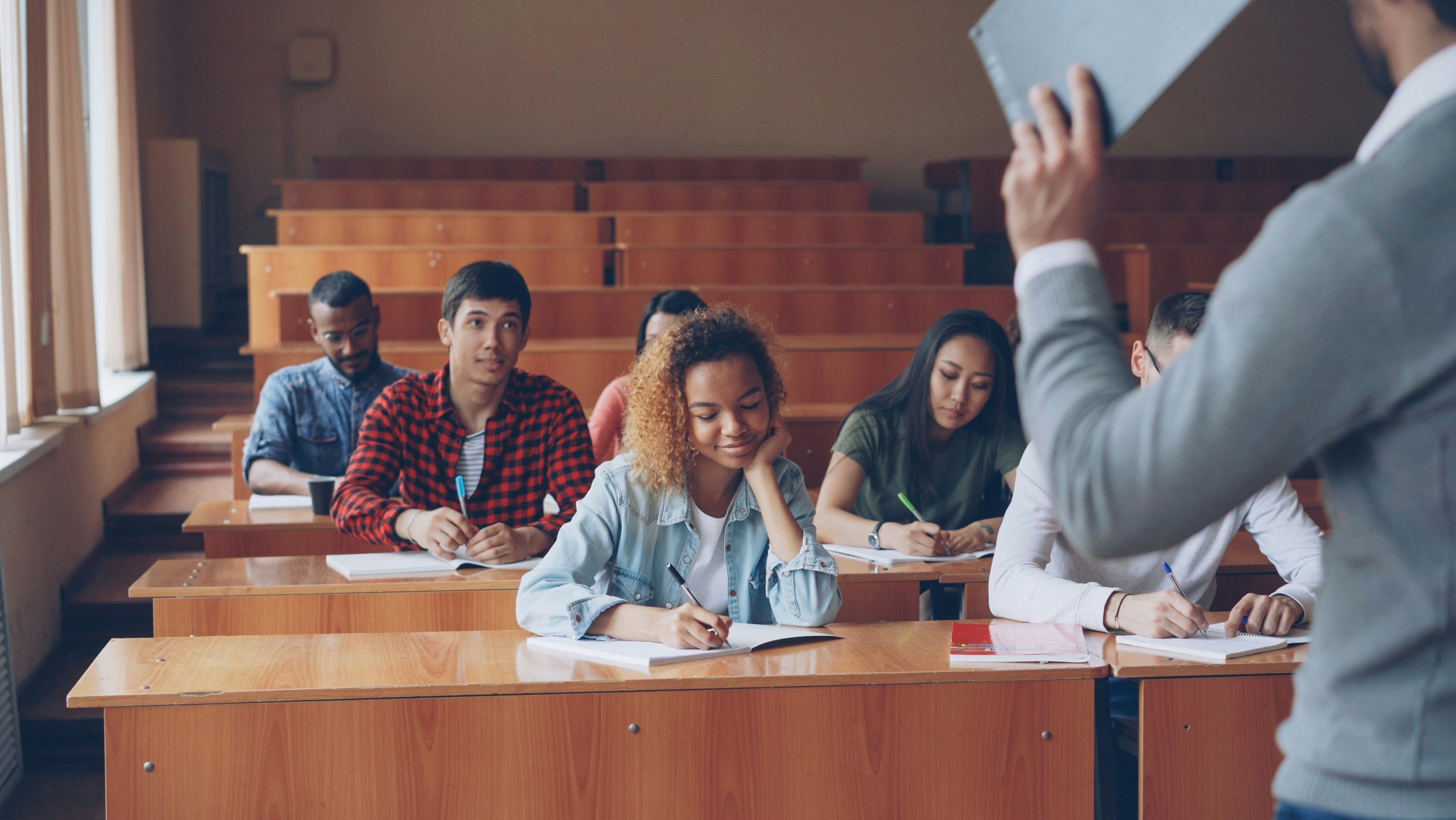 Students sitting in a classroom, taking notes, listening to a lecturer.