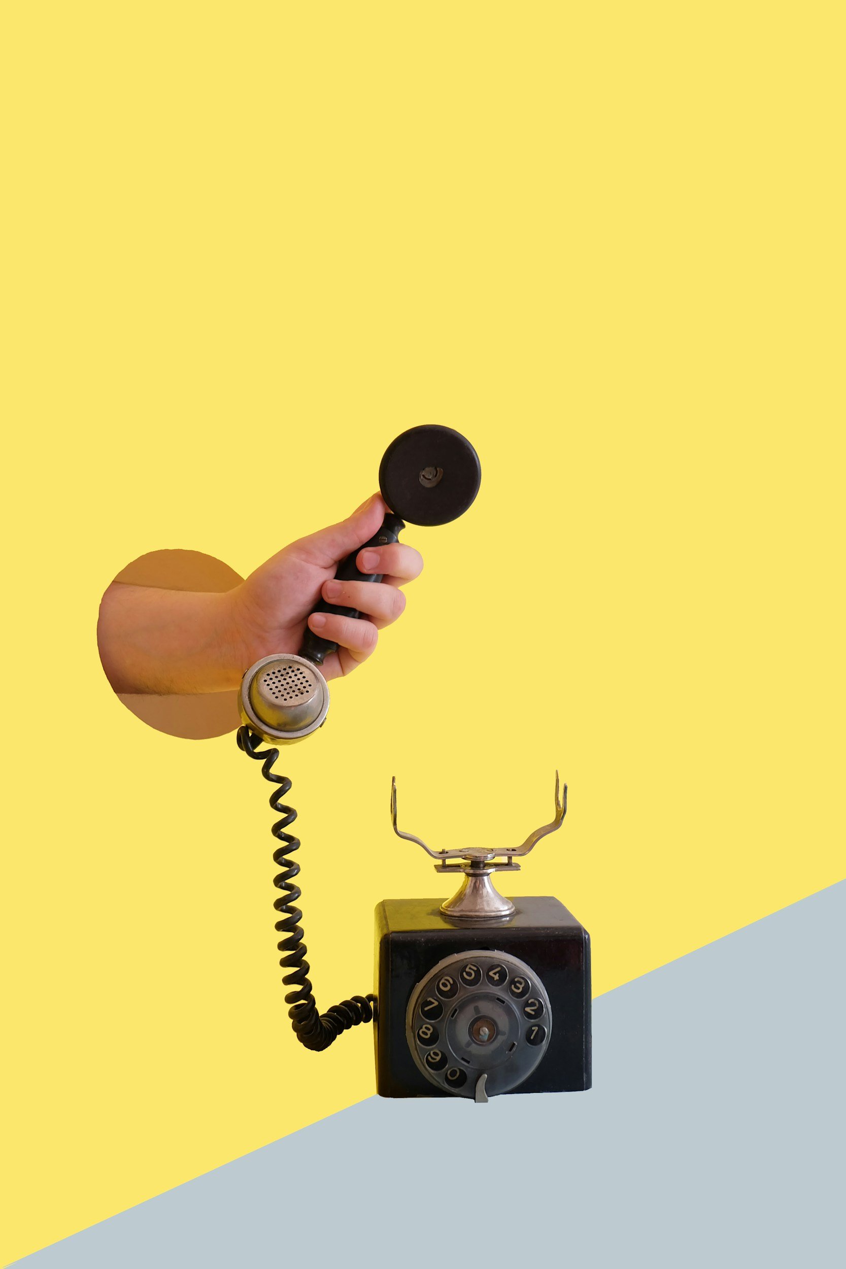 Vintage black rotary phone hanging on a sticky note with a small decorative reindeer figurine in the background on a yellow wall and a gray and yellow table.
