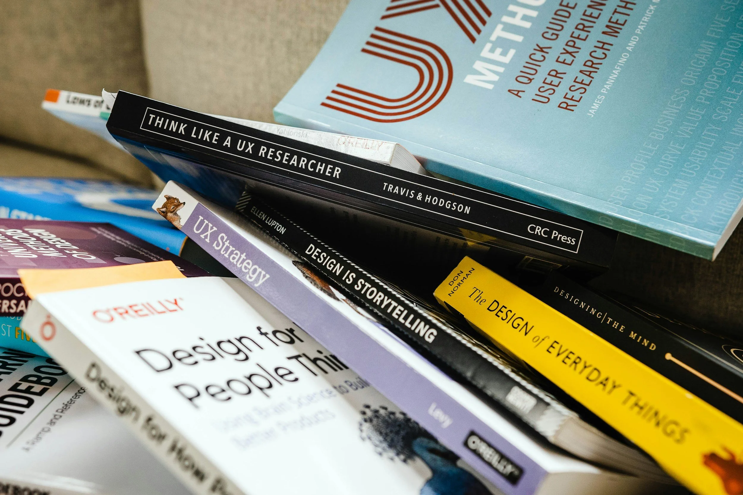 Close-up of a stack of books about design and UX research, including titles like 'Think Like a UX Researcher' and 'Designing the Mind'.