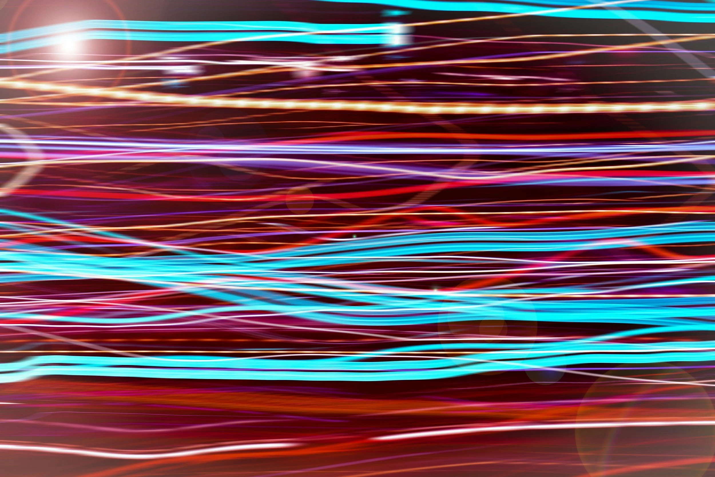 Long exposure photo of colorful streaks of light moving across the frame on a dark background.