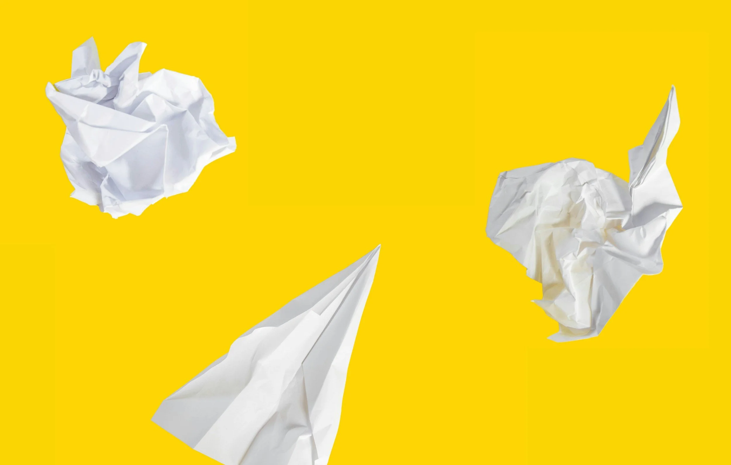 Several crumpled pieces of white paper on a bright yellow background.