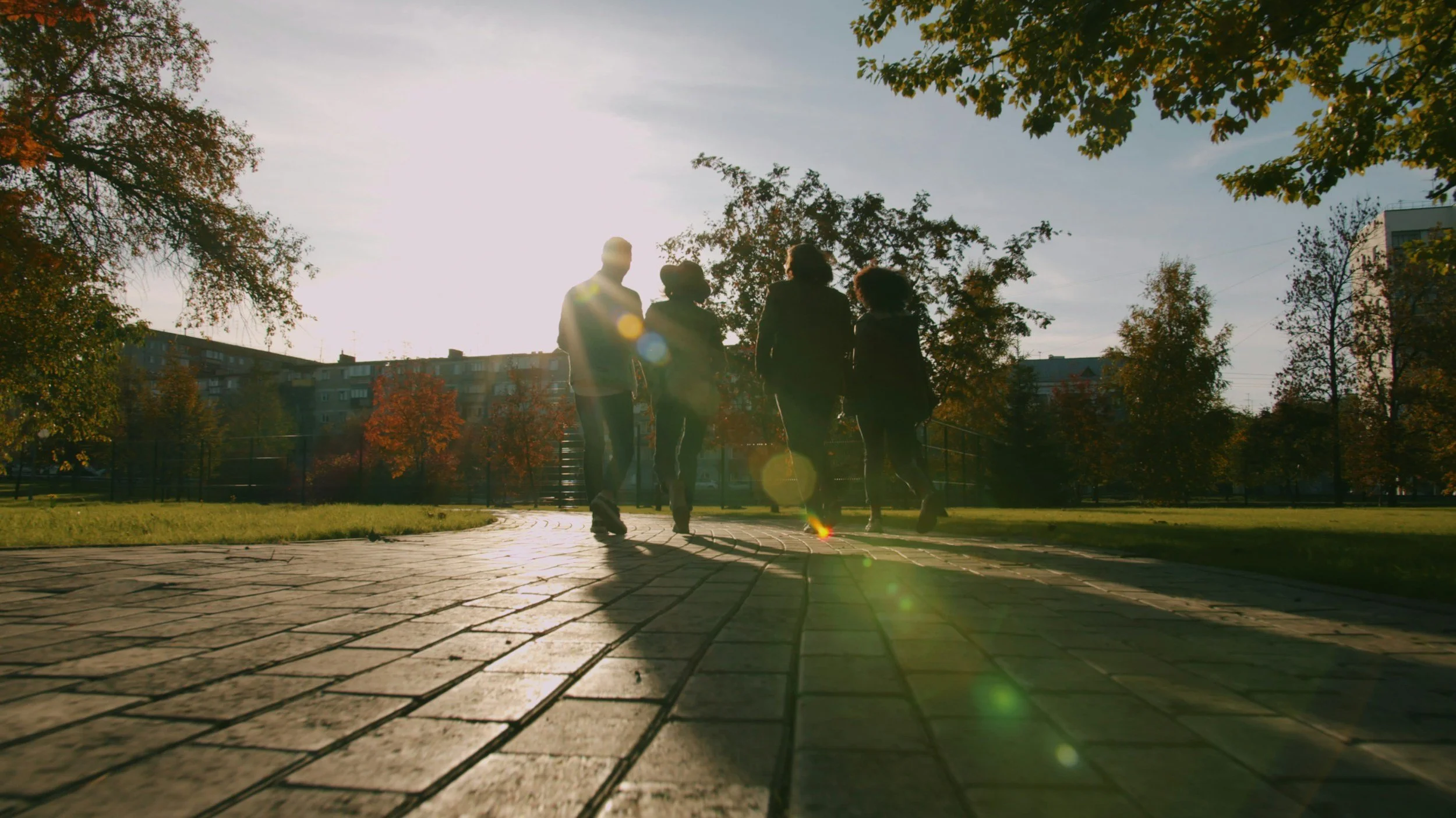 The silhouette back of four people walking  on a brick path and blurred by the sunlight