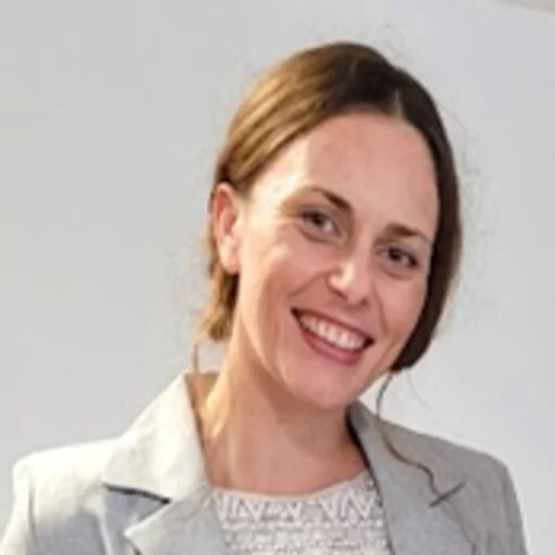 A woman with light brown hair and a gray blazer smiling at the camera.