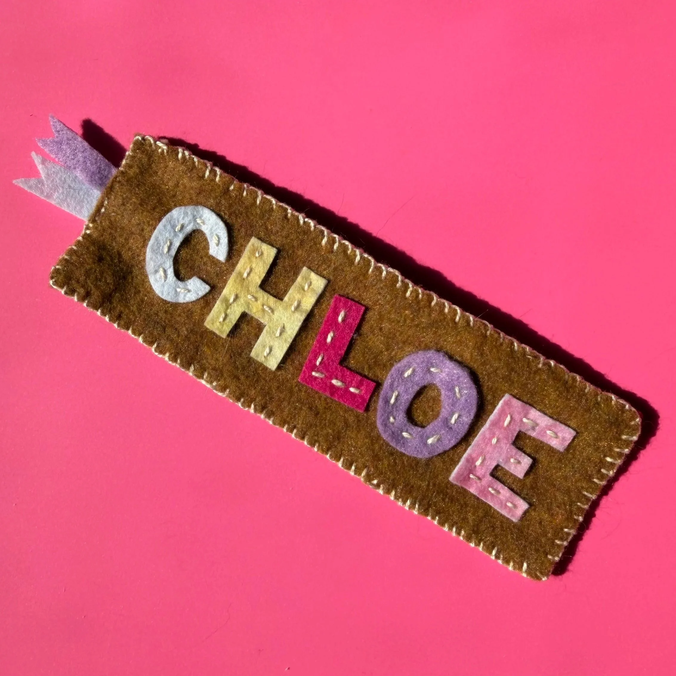 Close-up of a felt birthday banner with multicolored letters on a pink background.