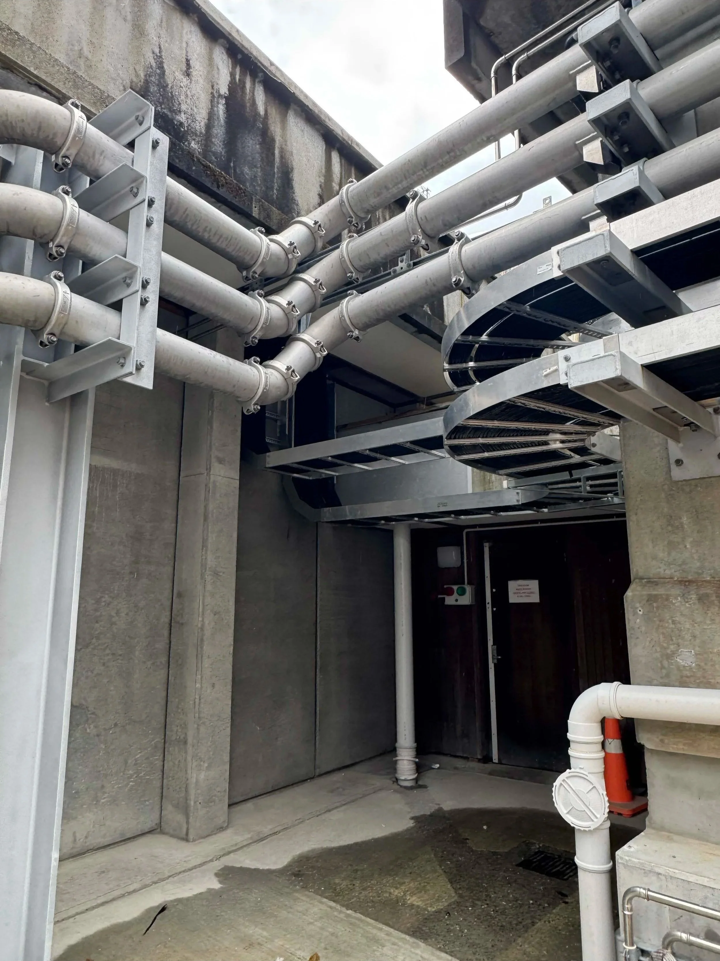 Pipes, encased electrical cords and conduit mounted on concrete walls of a building at Te Mārua Dissolved Air Flotation Plant, installed by Stewart Electrical.