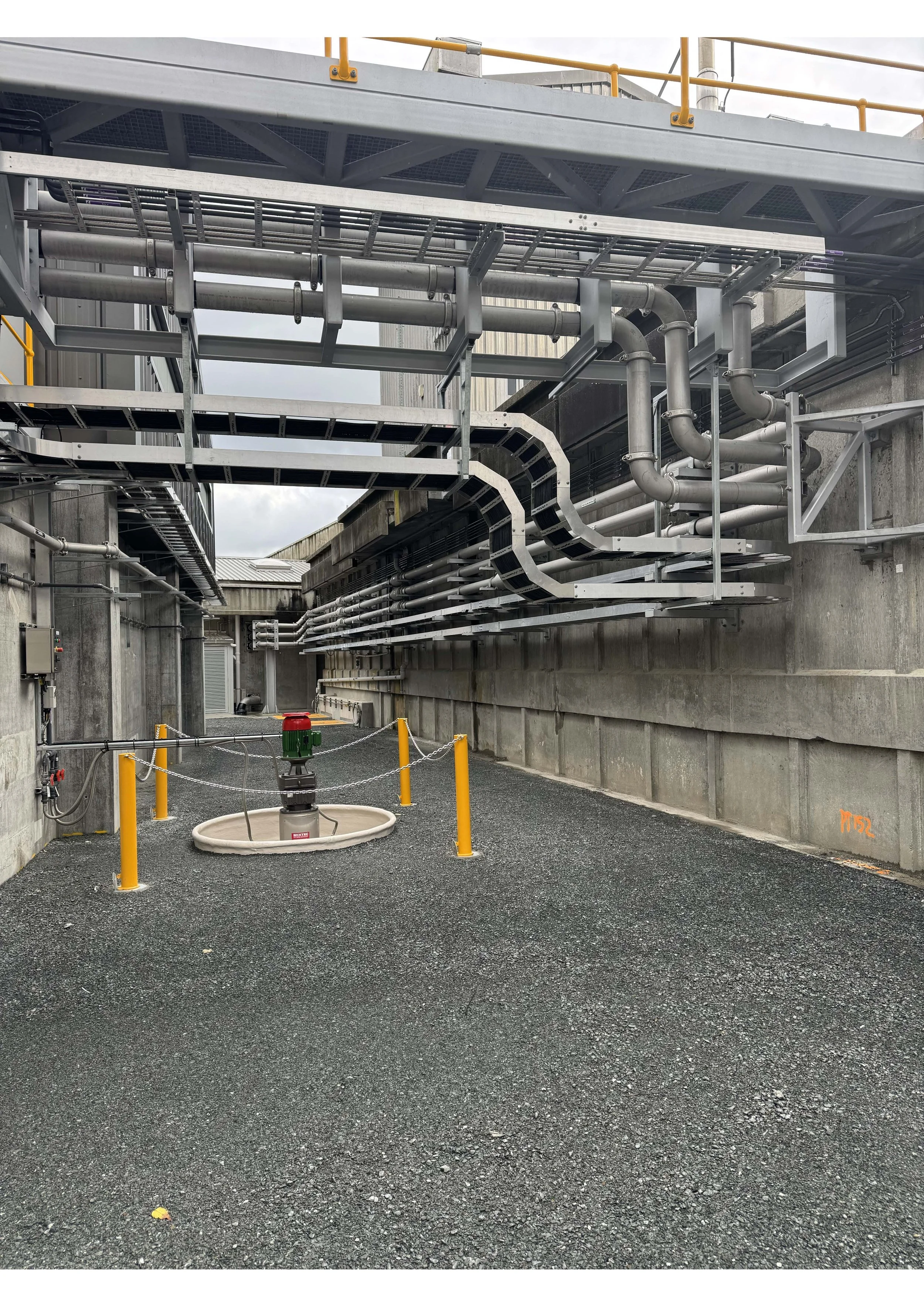 Industrial piping system with multiple pipes and valves mounted on the concrete walls outside a building with an open hatch with a green valve. Work done by Stewart Electrical at Te Mārua Dissolved Air Flotation Plant.