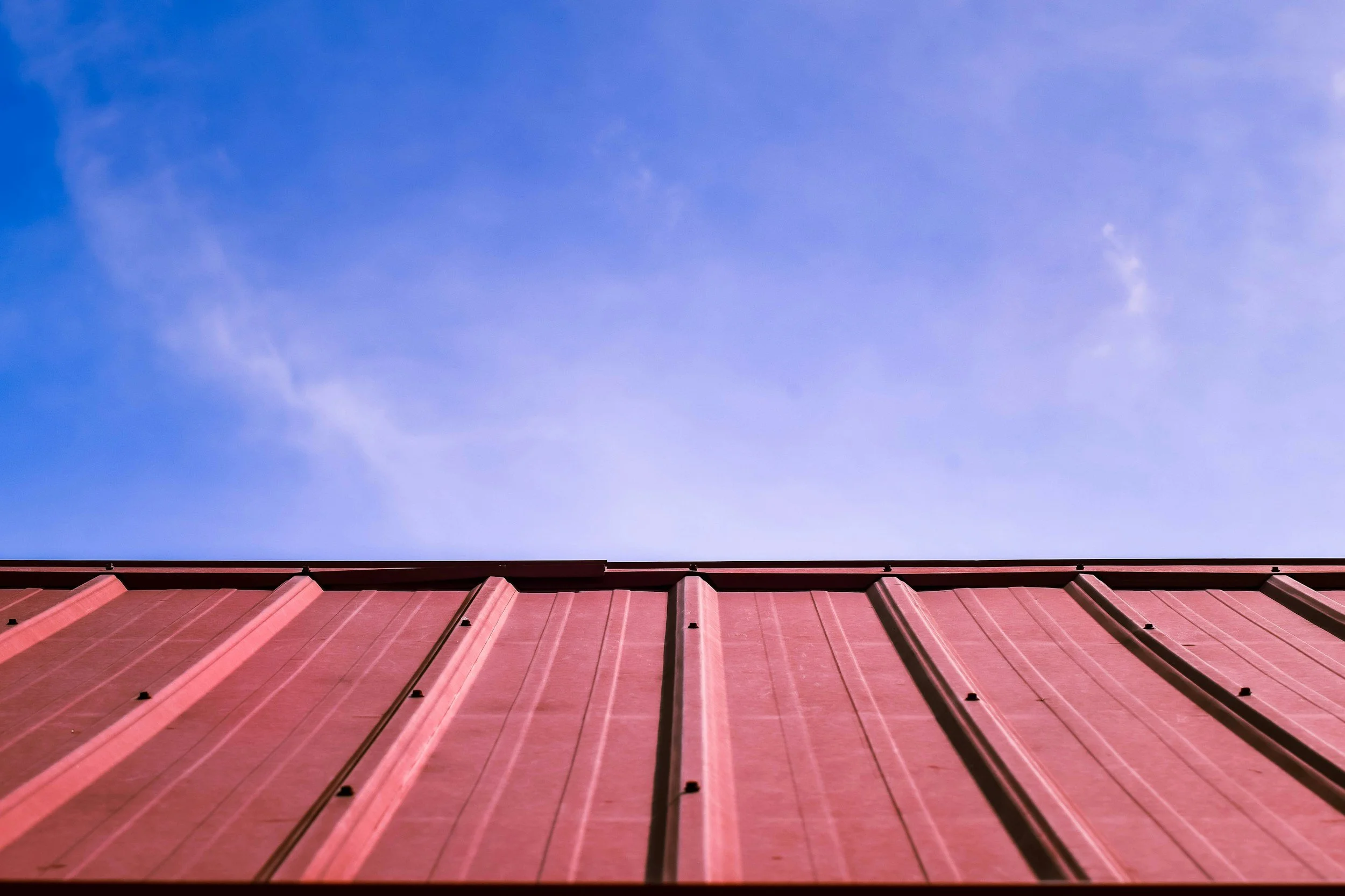 Vue du sommet d'une structure en tôle rouge sous un ciel bleu avec quelques nuages.