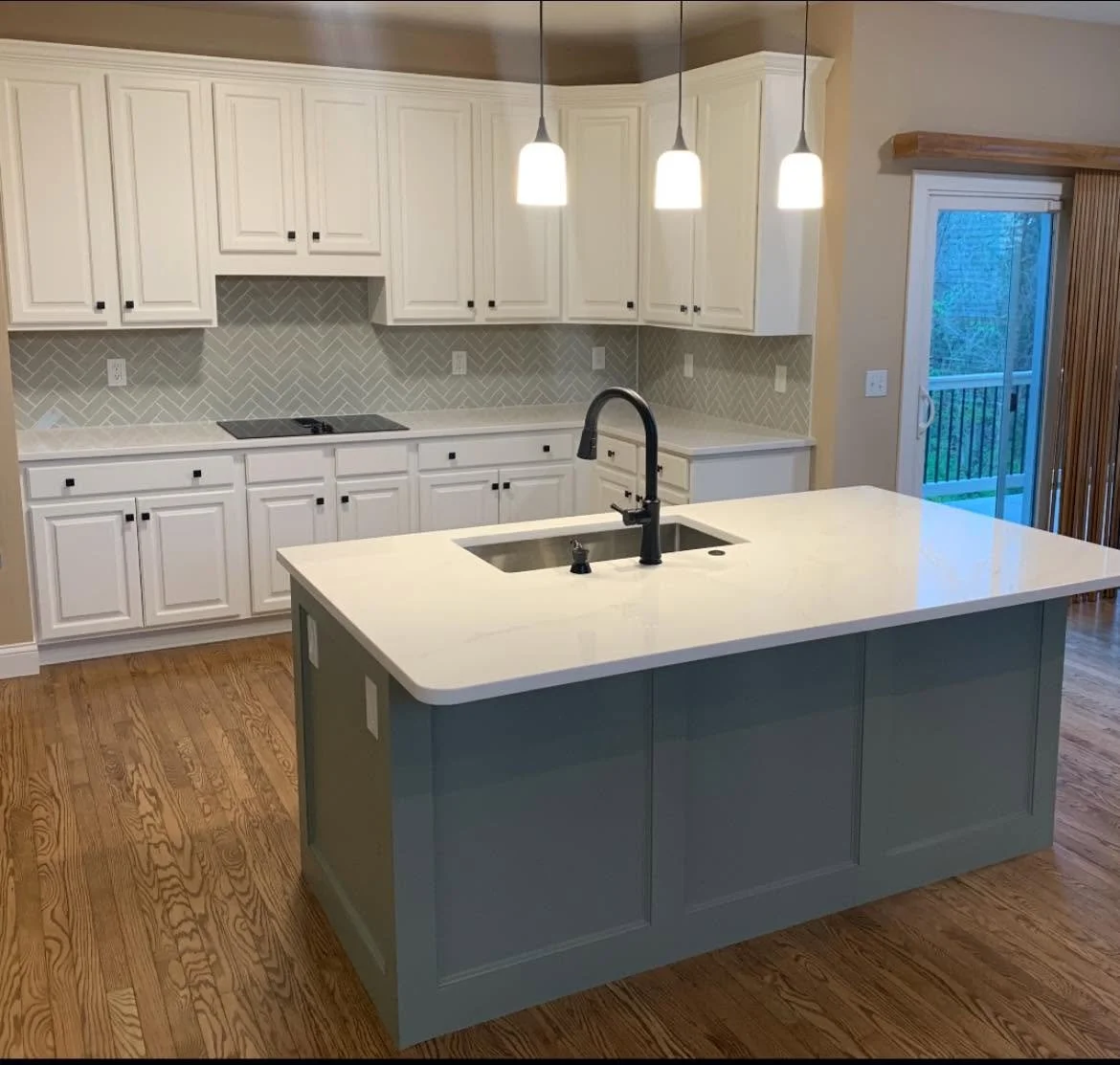 Modern kitchen with white cabinets, a large island with a white countertop, pendant lighting, a sliding glass door, and wood flooring.