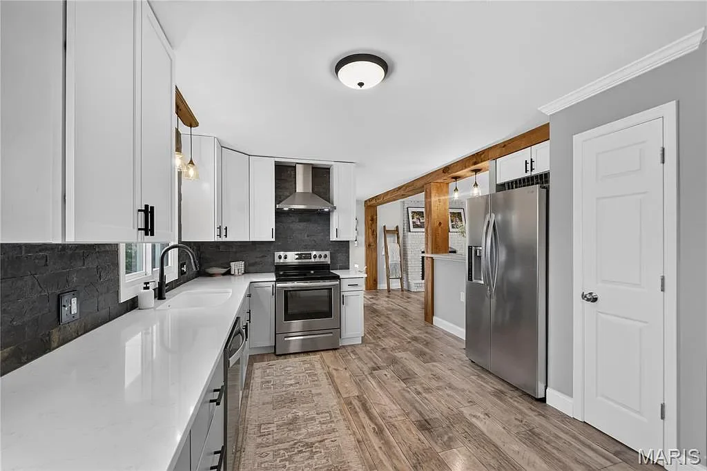 Modern kitchen with white cabinets, a black backsplash, stainless steel appliances including a refrigerator and oven, dark wood flooring, and a ceiling light fixture.