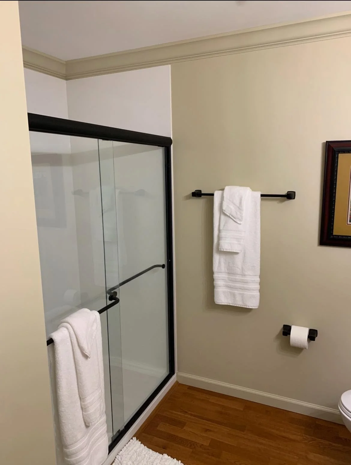 A bathroom with a glass shower door, a framed picture on the wall, and towel racks with white towels.