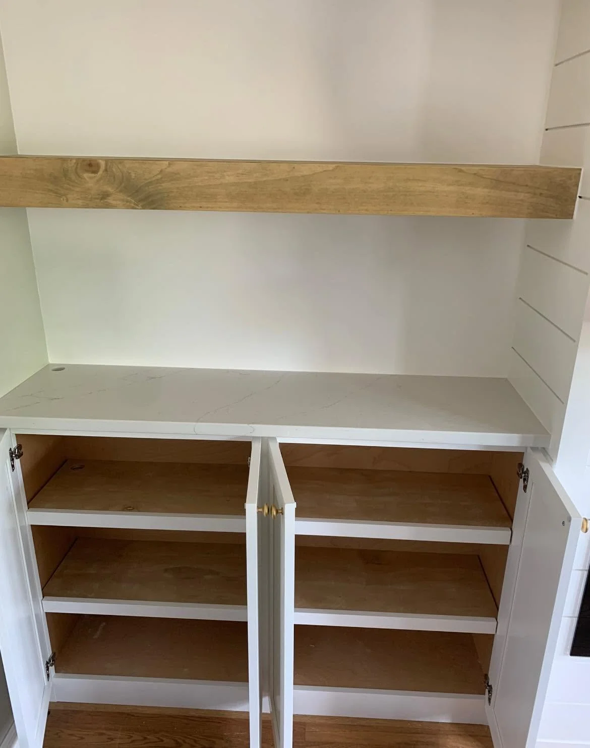 Empty white kitchen cabinet with four shelves and a wooden countertop inside.