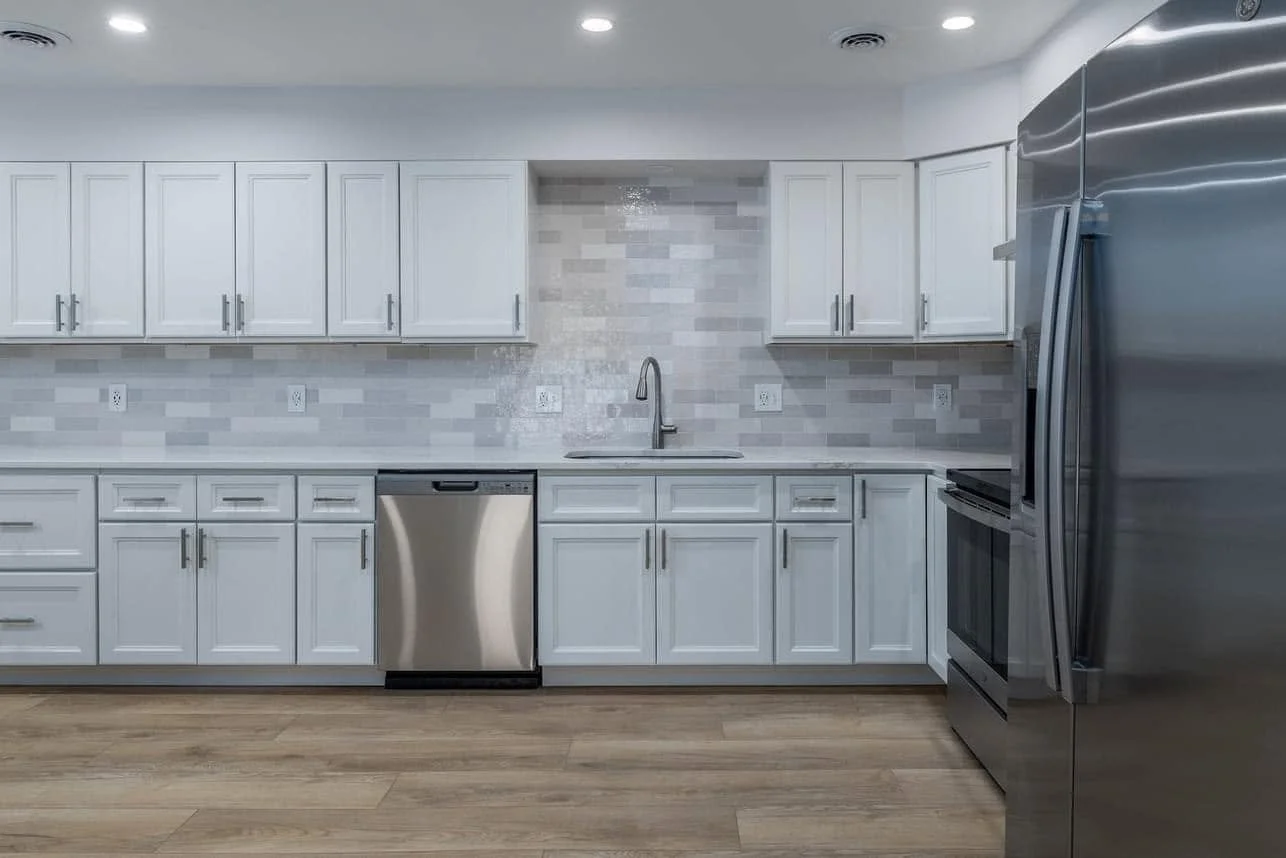 Modern kitchen with white cabinets, stainless steel appliances, a tile backsplash, and hardwood flooring.