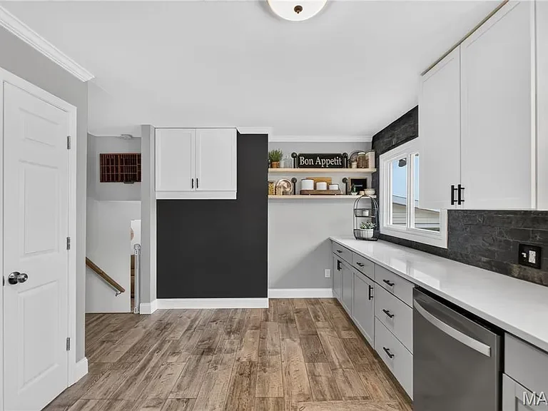 Modern kitchen with white cabinets, black and gray accents, wood flooring, and open shelving displaying decorative items and kitchenware.