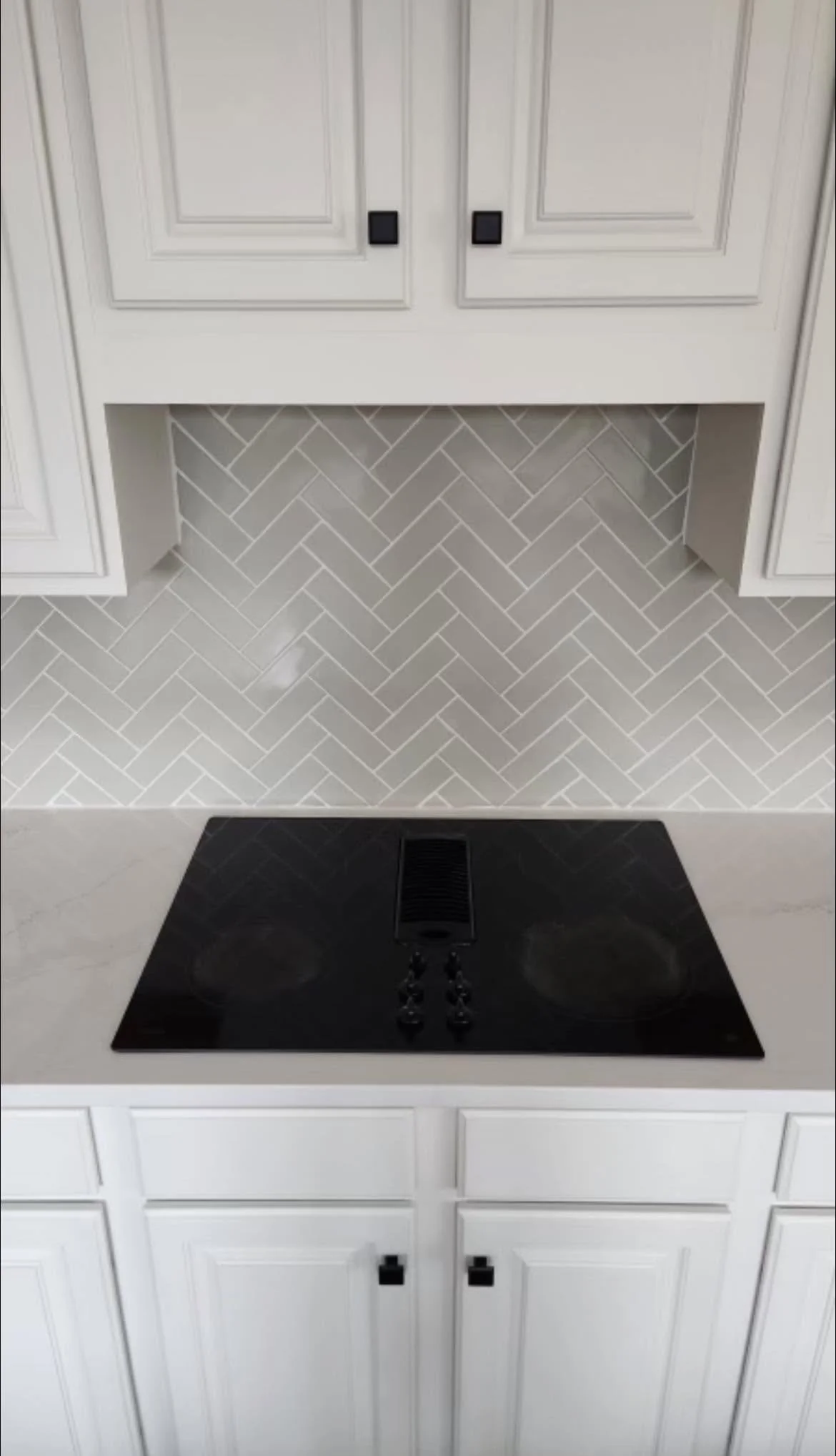 Kitchen with white cabinets, a black stovetop, herringbone-patterned tile backsplash, and a floor vent.