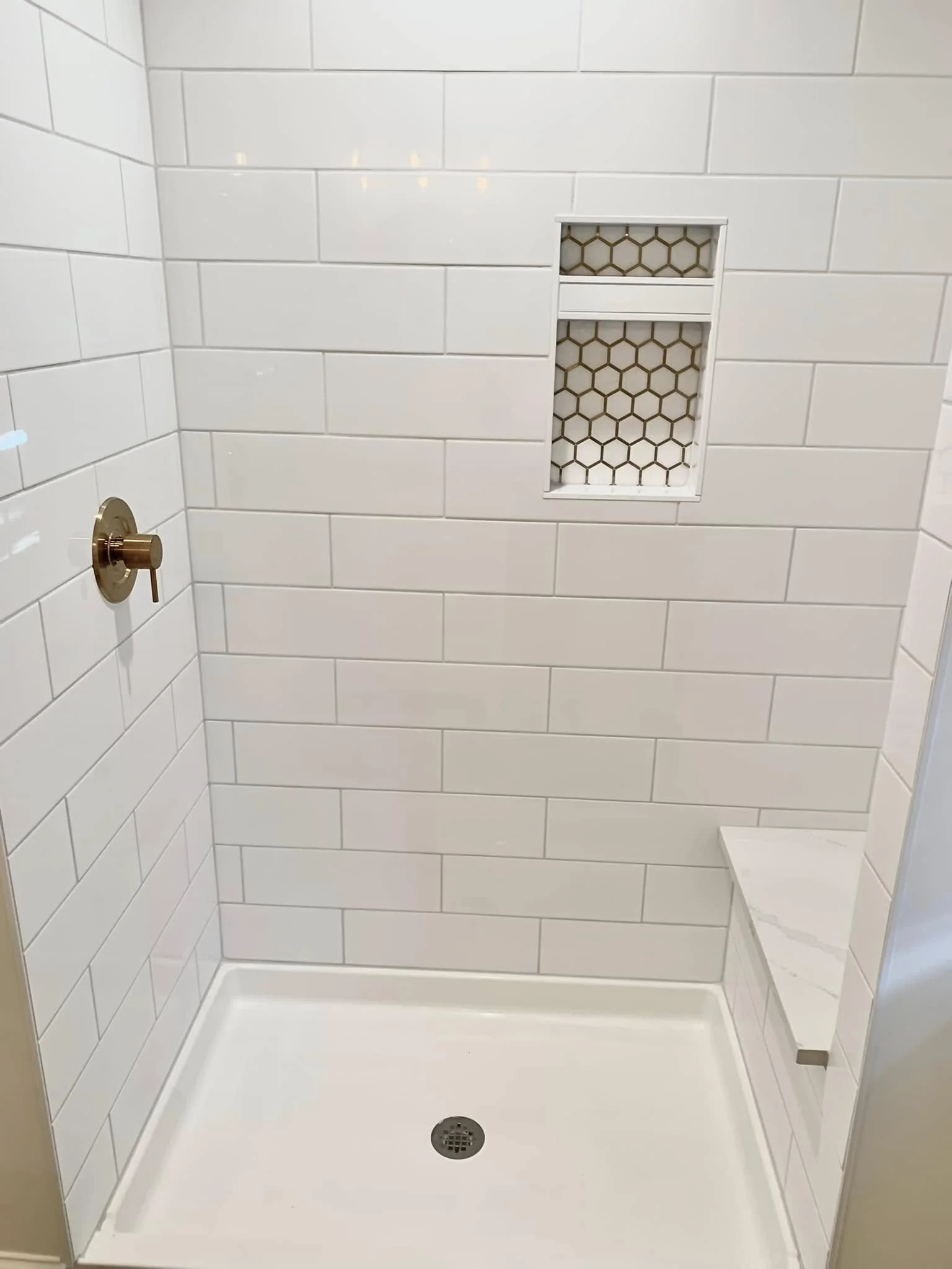 Empty walk-in shower with white subway tile walls, a built-in tiled niche, a white shower base, and a brass shower valve.