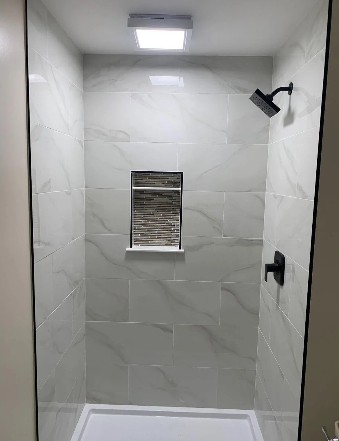 Modern shower with marble tiles, a small window with mosaic tile border, and black fixtures including a showerhead and handle.