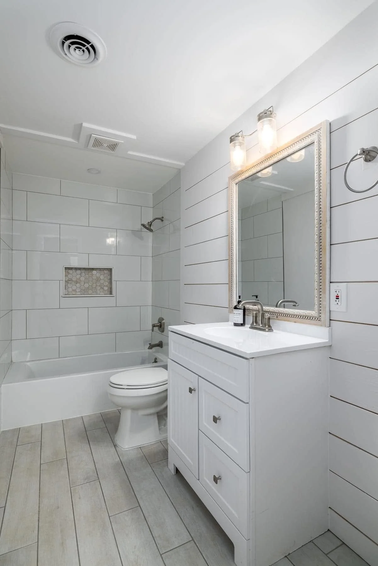 White bathroom with bathtub, toilet, and vanity with mirror and lights.