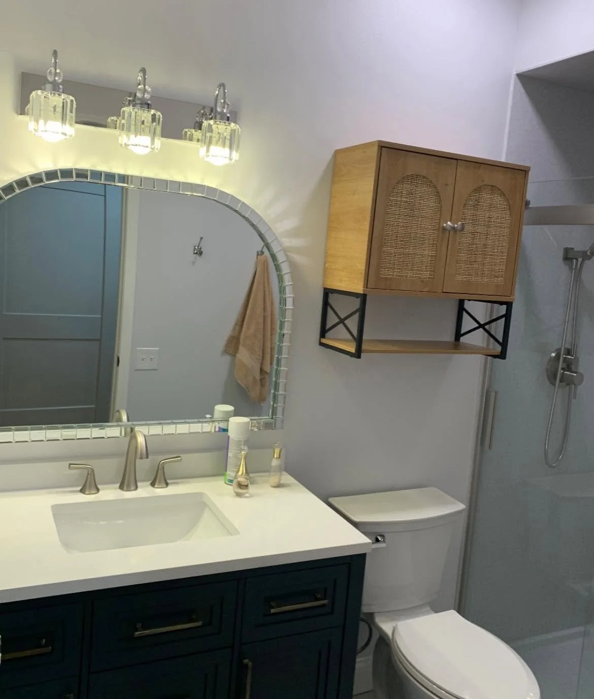 Bathroom with a mirror, vanity with faucet, soap and lotion bottles, a toilet, wall cabinet, and shower with a handheld showerhead.