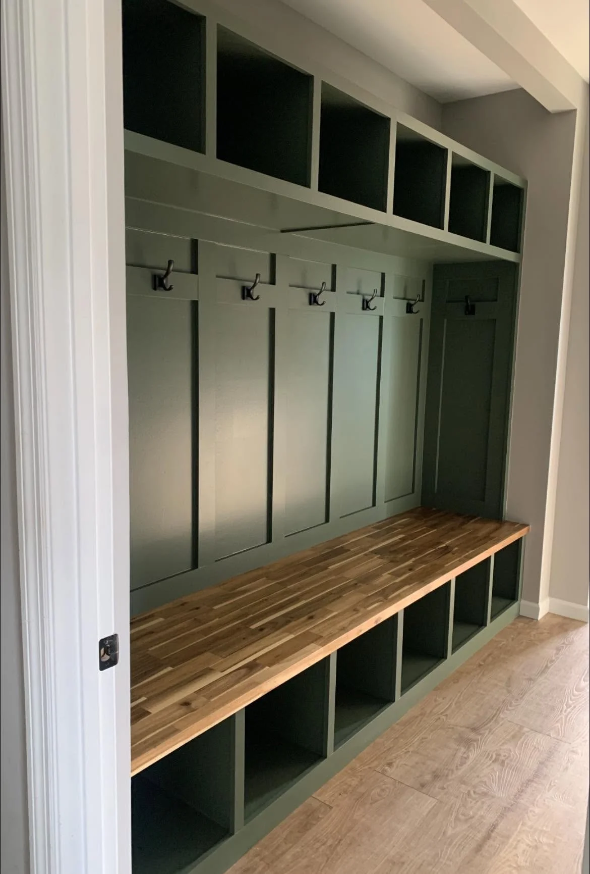 Entryway with green built-in storage unit featuring hooks, cubbies, and a wooden bench.