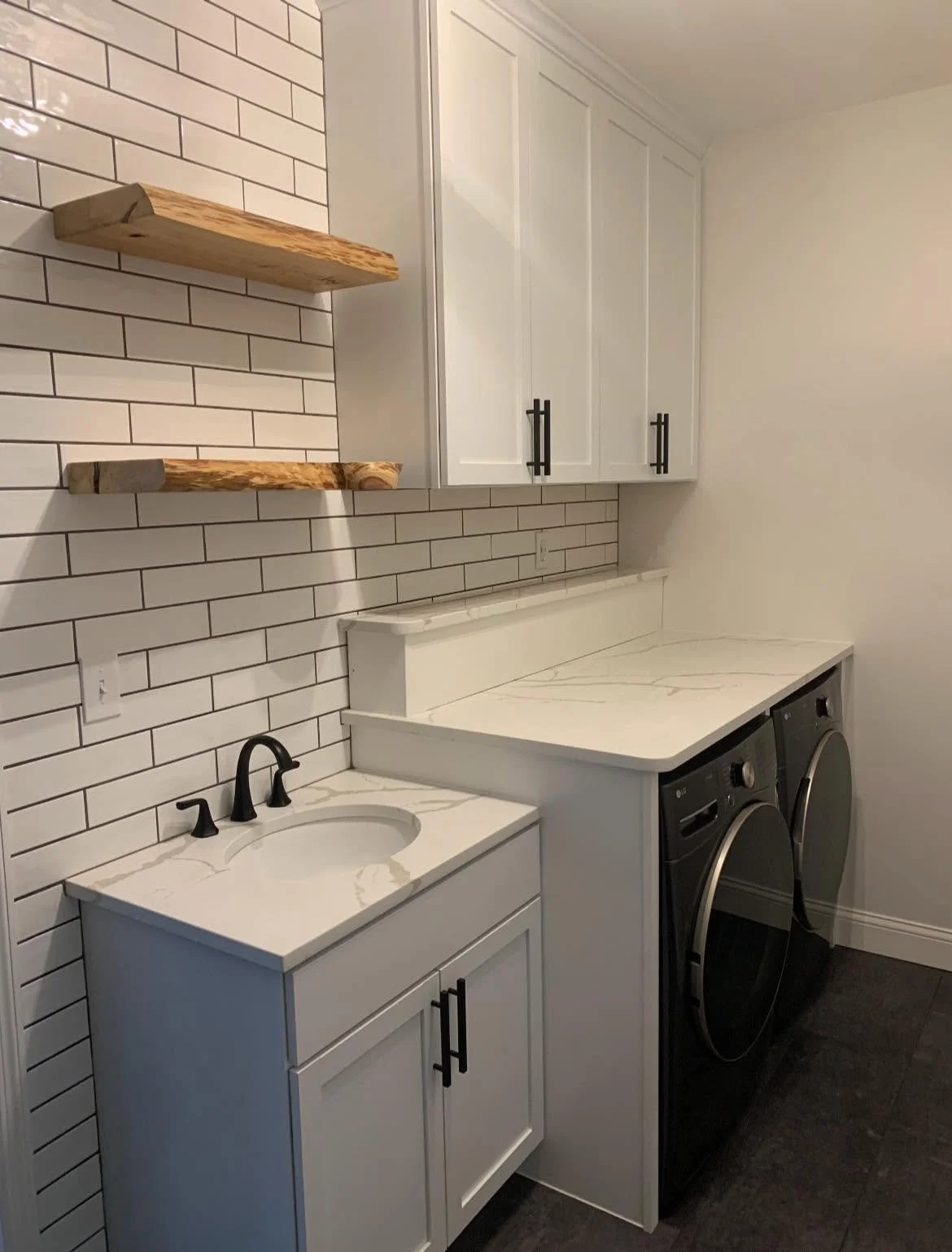 Laundry room with white cabinets, a small sink with black faucet, wooden shelves on brick wallpaper wall, and a washer and dryer.