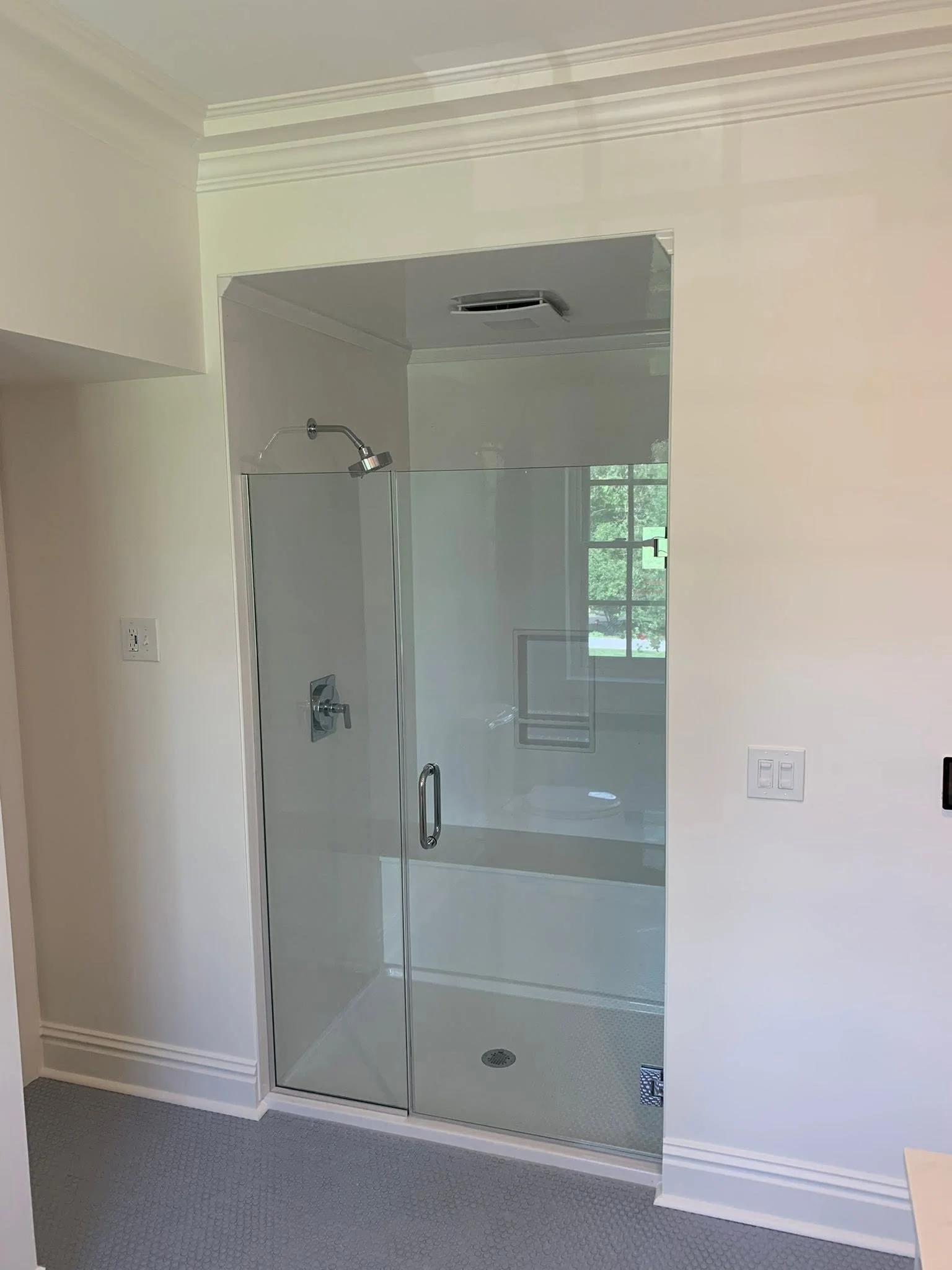 Modern bathroom with a glass-enclosed shower stall, chrome fixtures, a window, and light-colored walls.