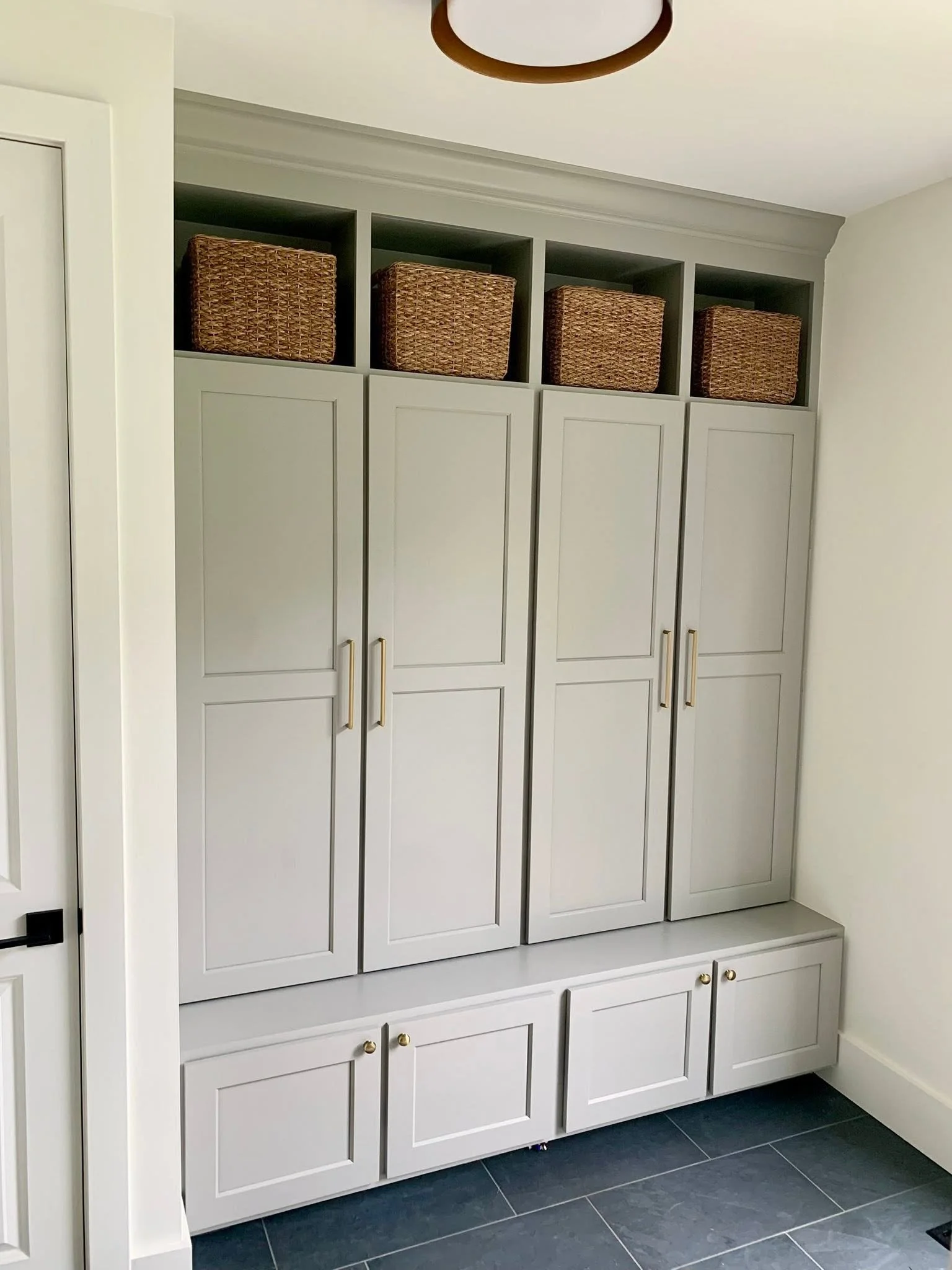 White cabinetry with closed doors, gold handles, and woven baskets above on open shelves in a room with dark tiled floor.