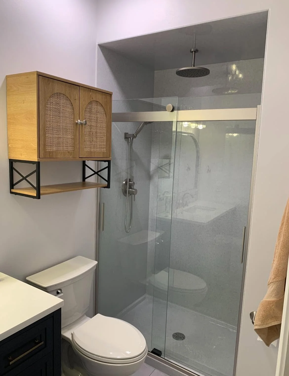 Small modern bathroom with a glass shower enclosure, gray shower wall, black vanity, toilet, and a wooden wall shelf with storage cabinets mounted on the wall.