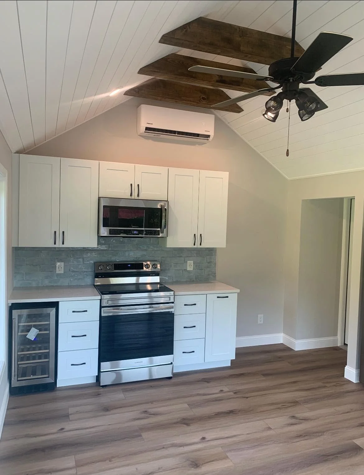 Kitchen with white cabinets, stainless steel microwave and stove, gray tile backsplash, mini wine cooler, ceiling fan, and HVAC system on the sloped ceiling.