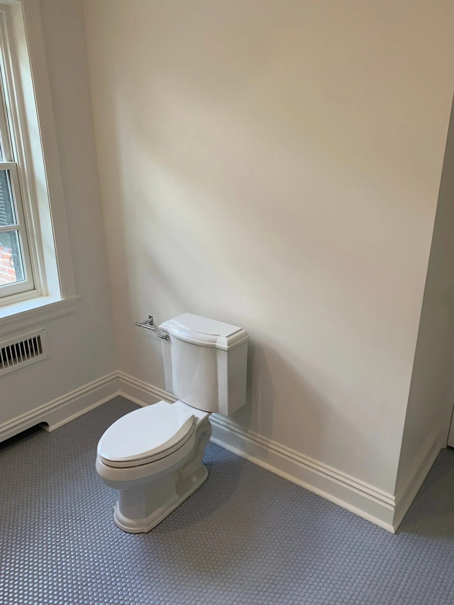 A bathroom with a white toilet, a window on the left, and beige walls.
