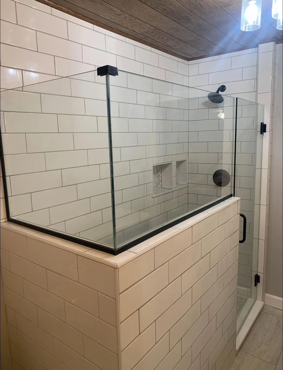 A bathroom shower with white subway tiles, a glass enclosure, a black showerhead, and two built-in niches for toiletries, adjacent to a white tiled wall.