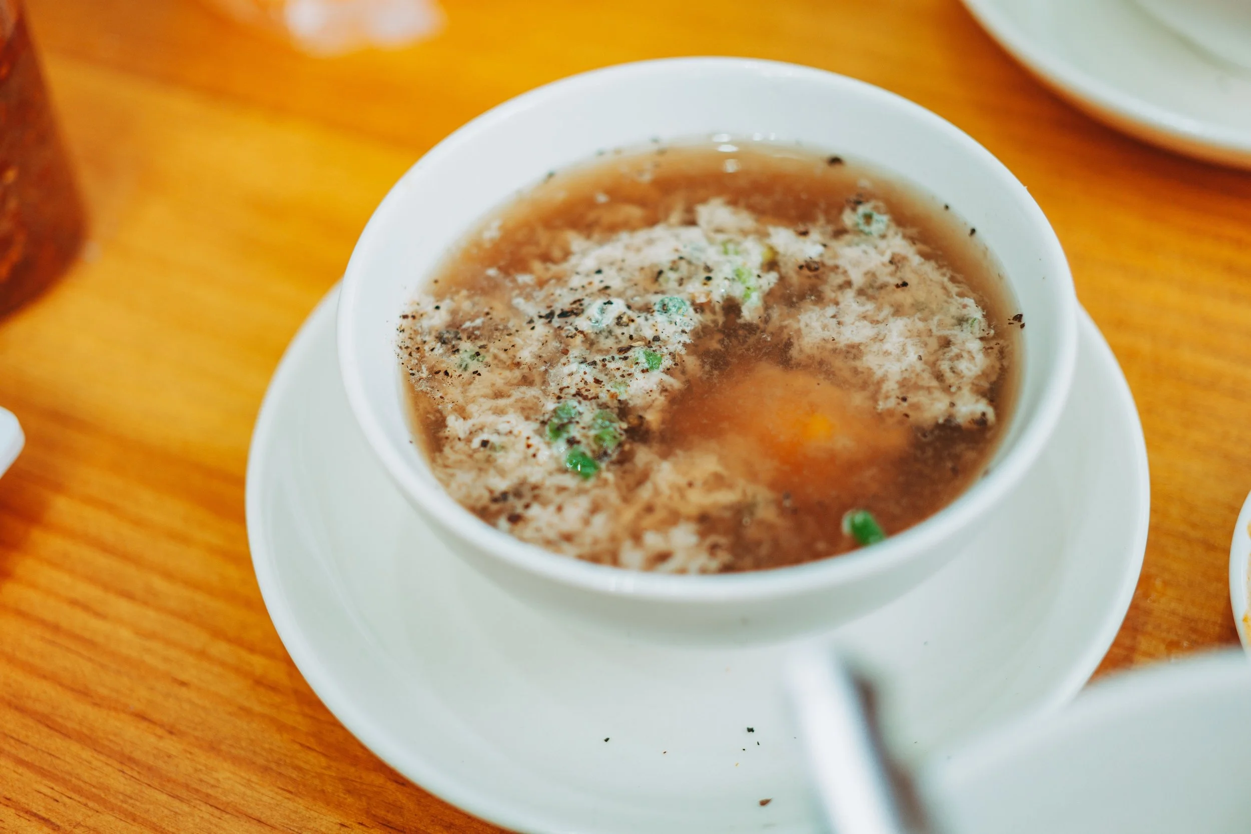 Cup of hot tea or broth with herbs and spices on a wooden table, with other dishes partially visible.