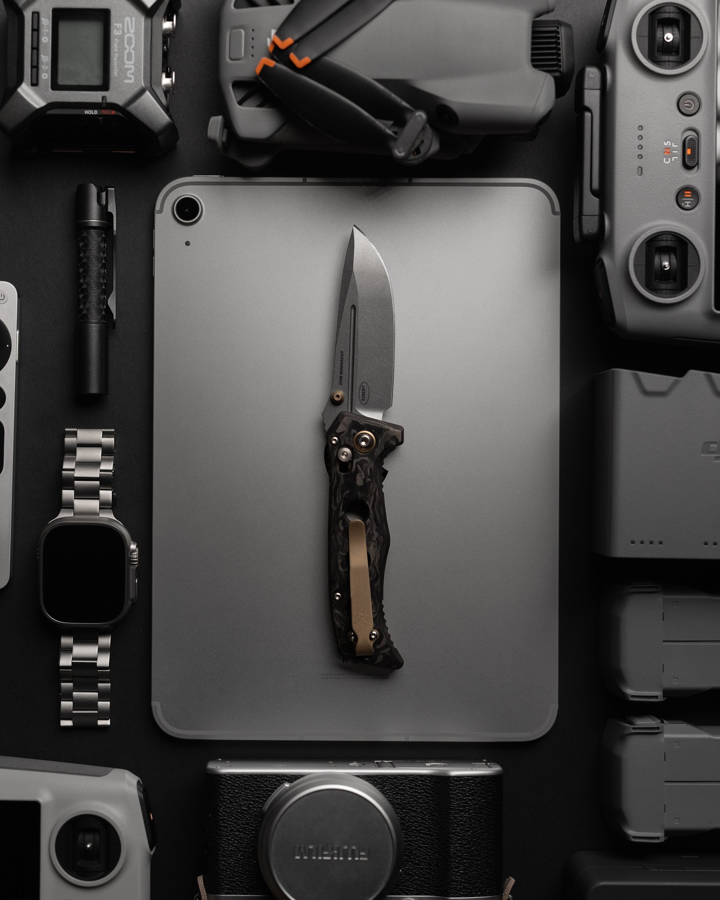 A flat lay of various photography and tech gadgets including a camera, drone, smartphone, microphone, hand knife, remote control, and other electronic devices.