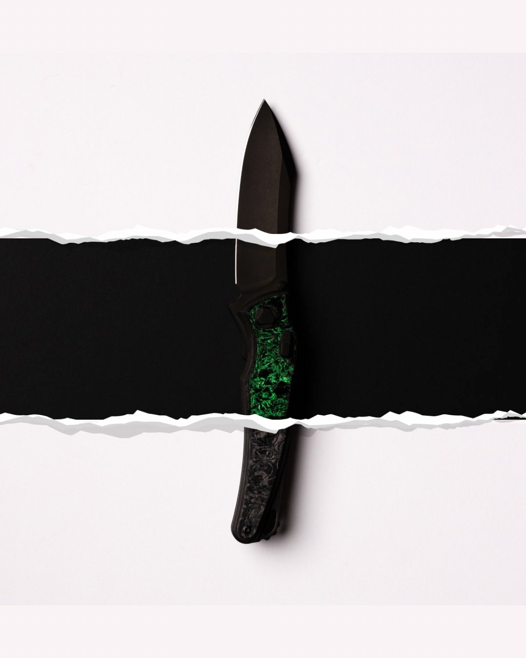 A black pocket knife with a green pattern handle and a black blade, partially hidden above and below torn white paper layers.