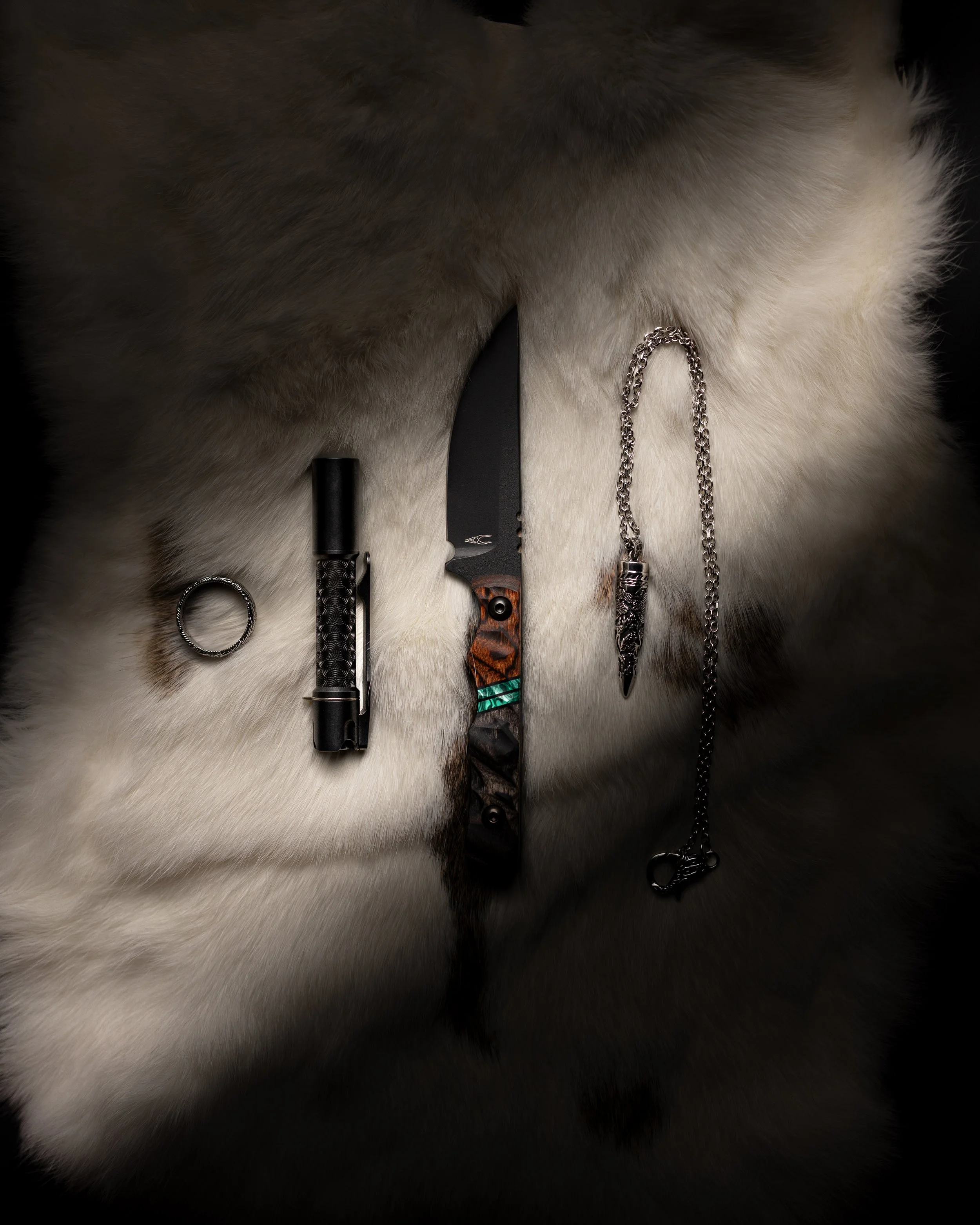 Close-up of a gray and white animal fur background with collection of knives and other metal objects placed on it.