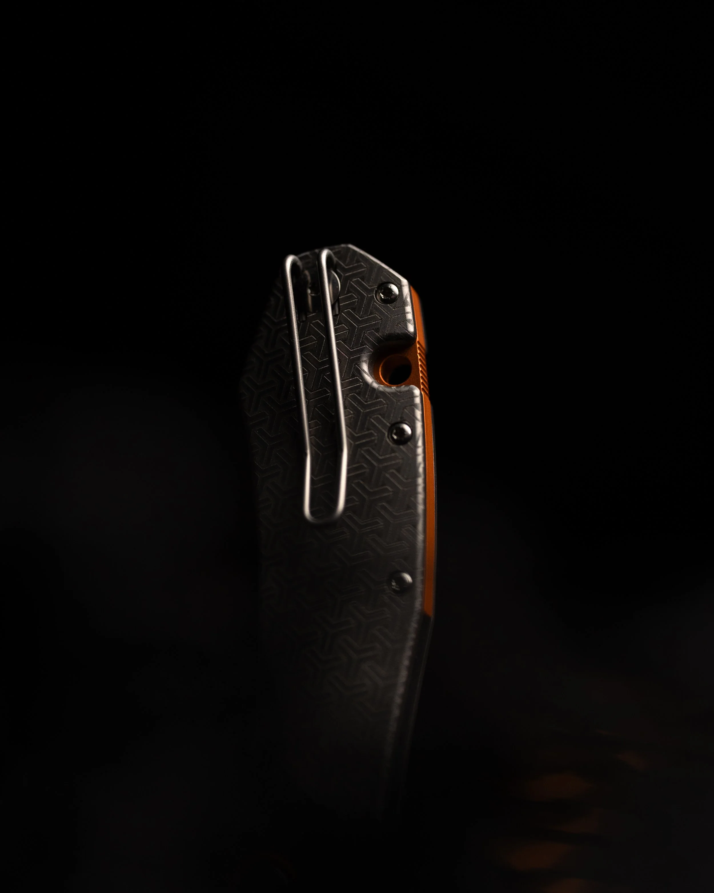 Close-up of a climbing or multi-tool with a textured black handle, metal clips, and orange accents, against a black background.