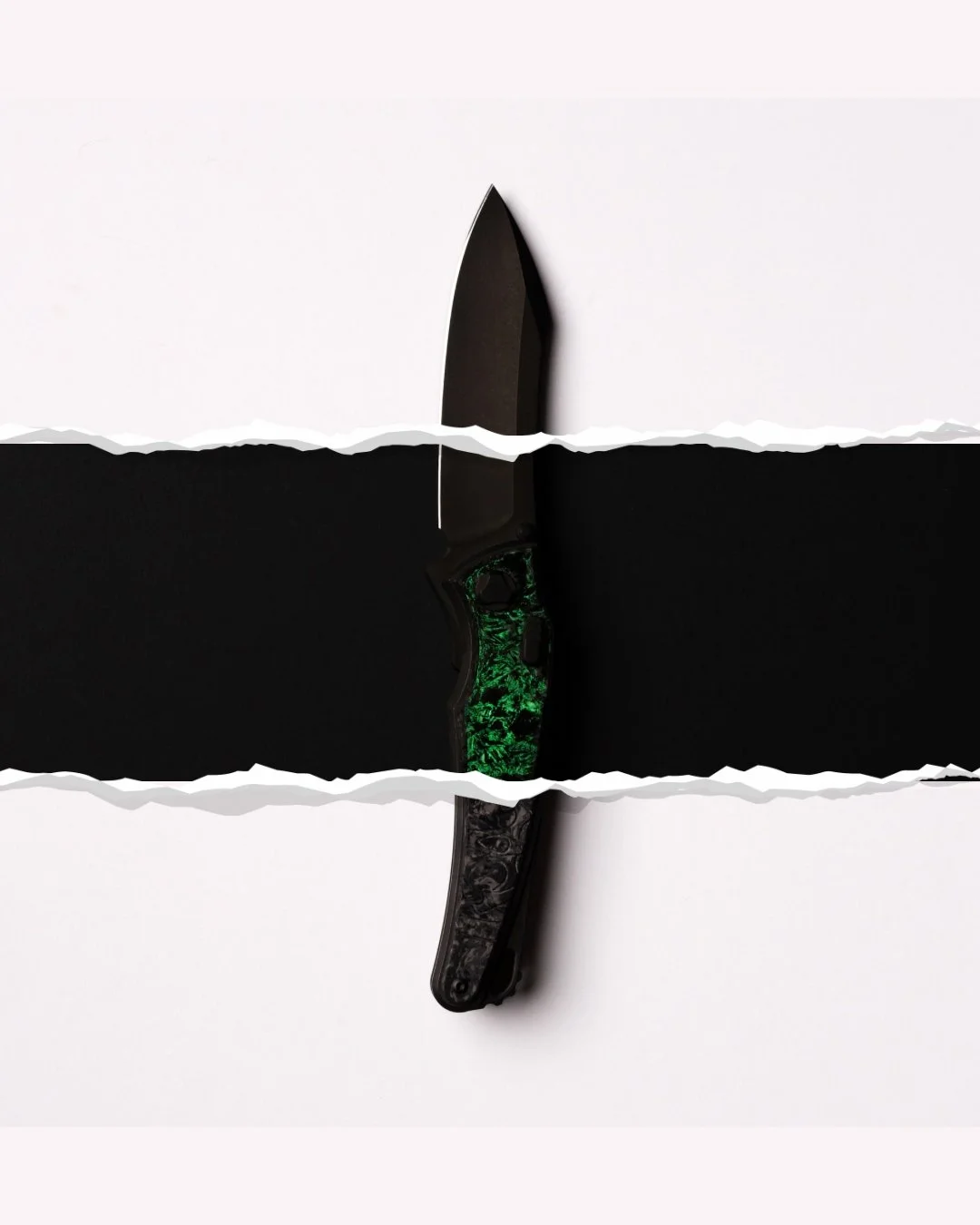 A black tactical knife with a green patterned handle, positioned vertically between two torn sections of white and black paper.