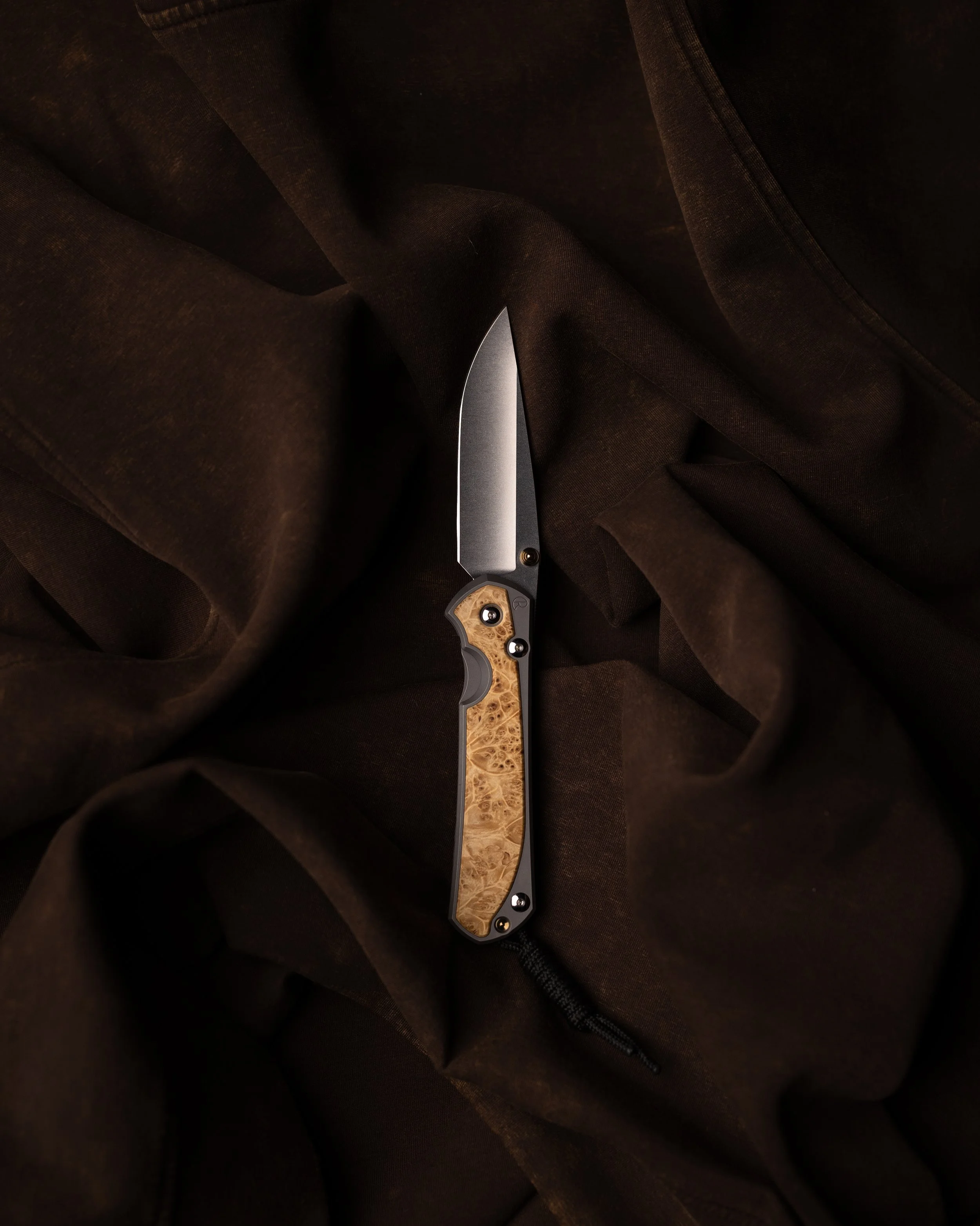 Close-up of a folding knife with a wooden handle, partially embedded in dark fabric