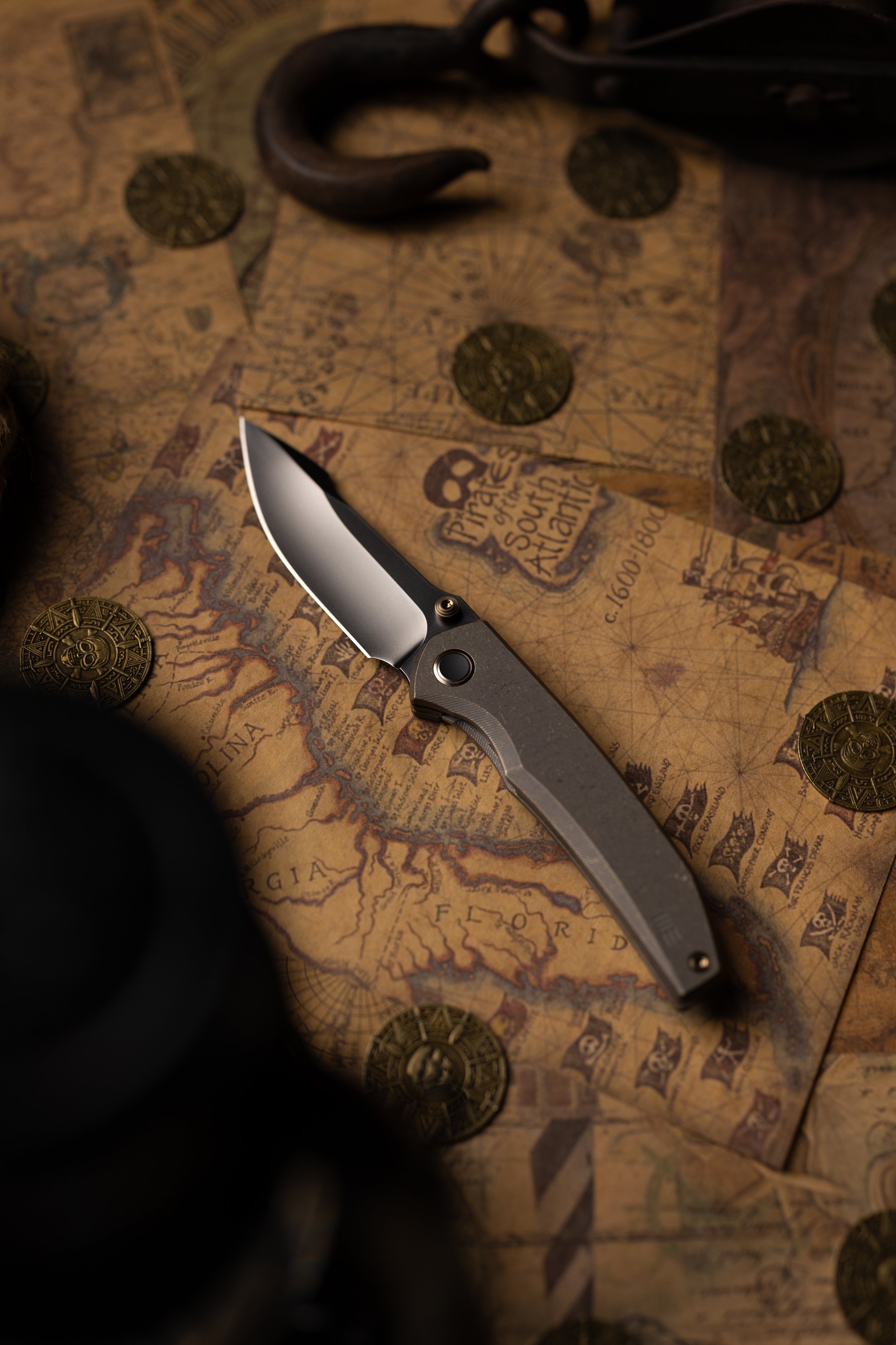 Close-up of a pirate-style map with scattered coins and a folding knife with a partially bent blade.