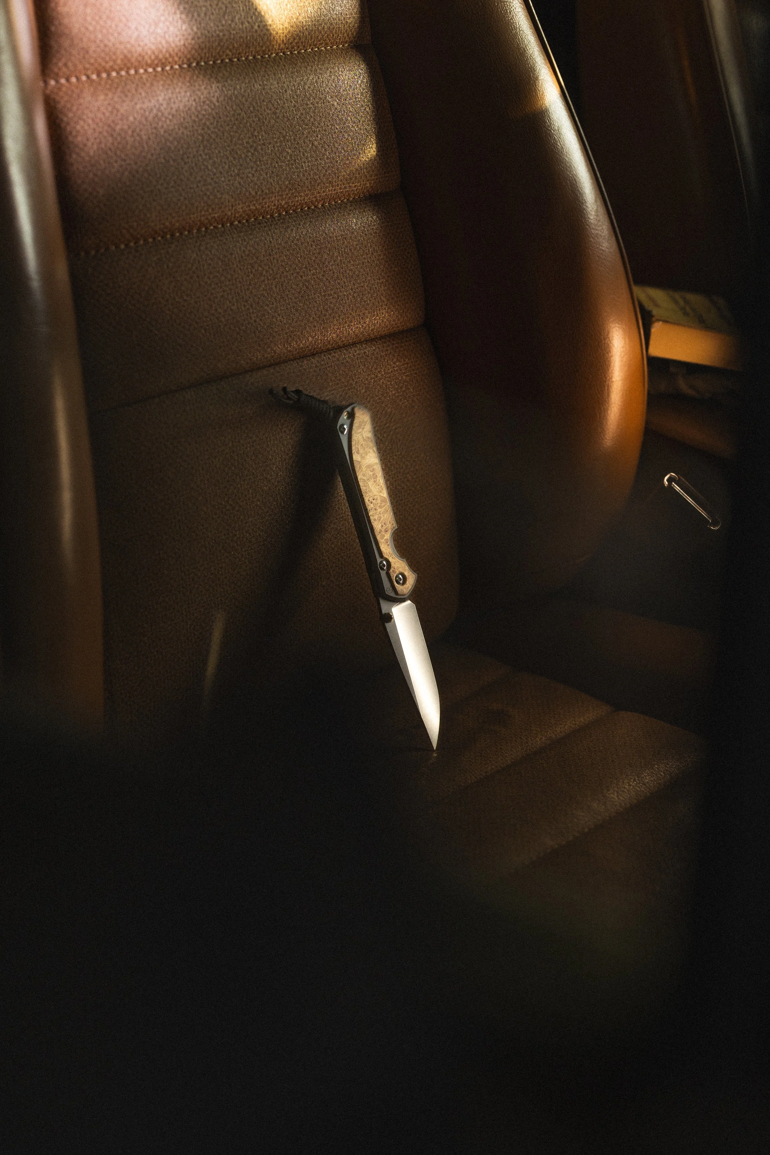 Inside a car, showing a brown leather seat and a switchblade knife resting on the seat.