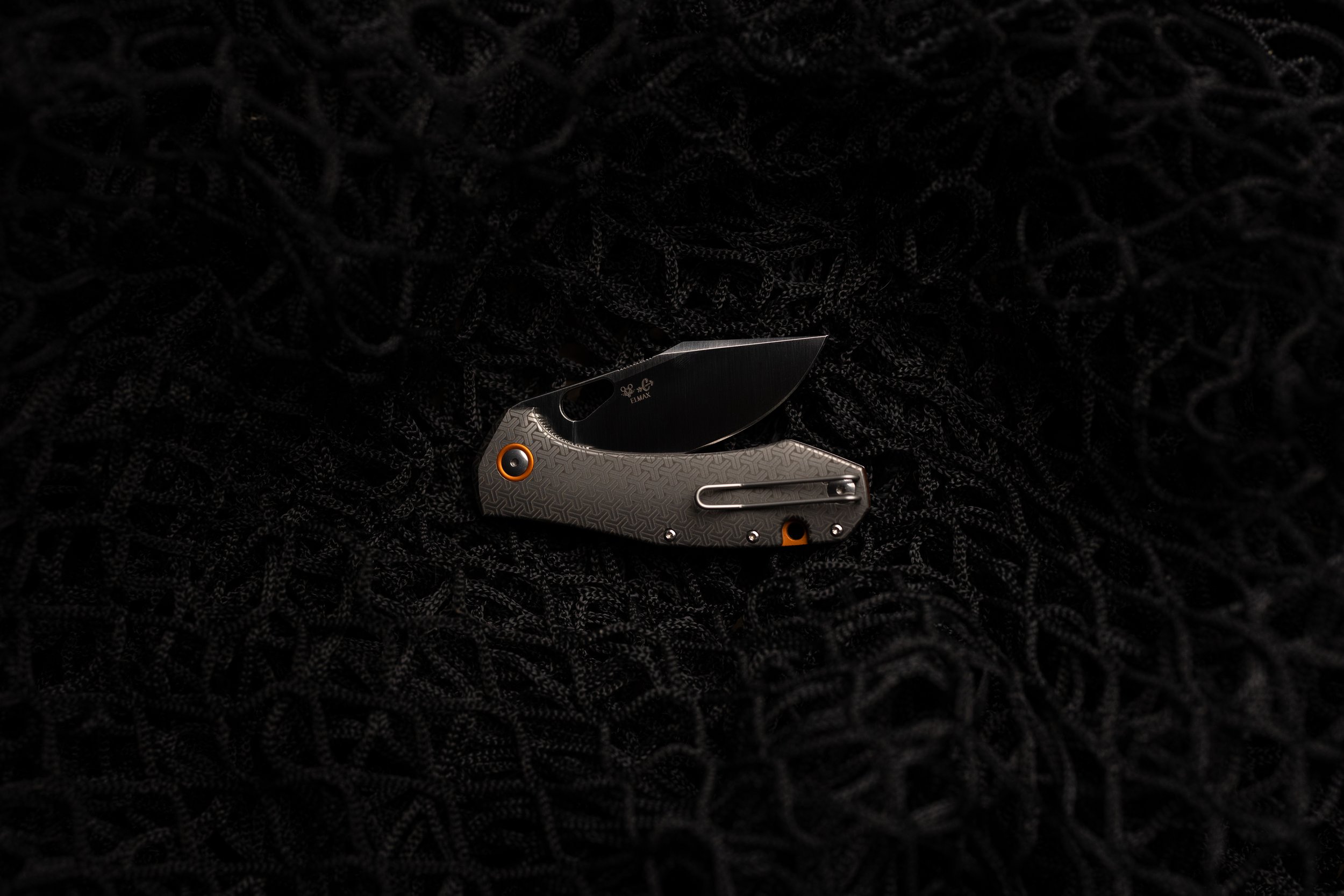 Close-up of a folding pocket knife with a textured grey handle and a black blade, resting on a black, textured fabric background.