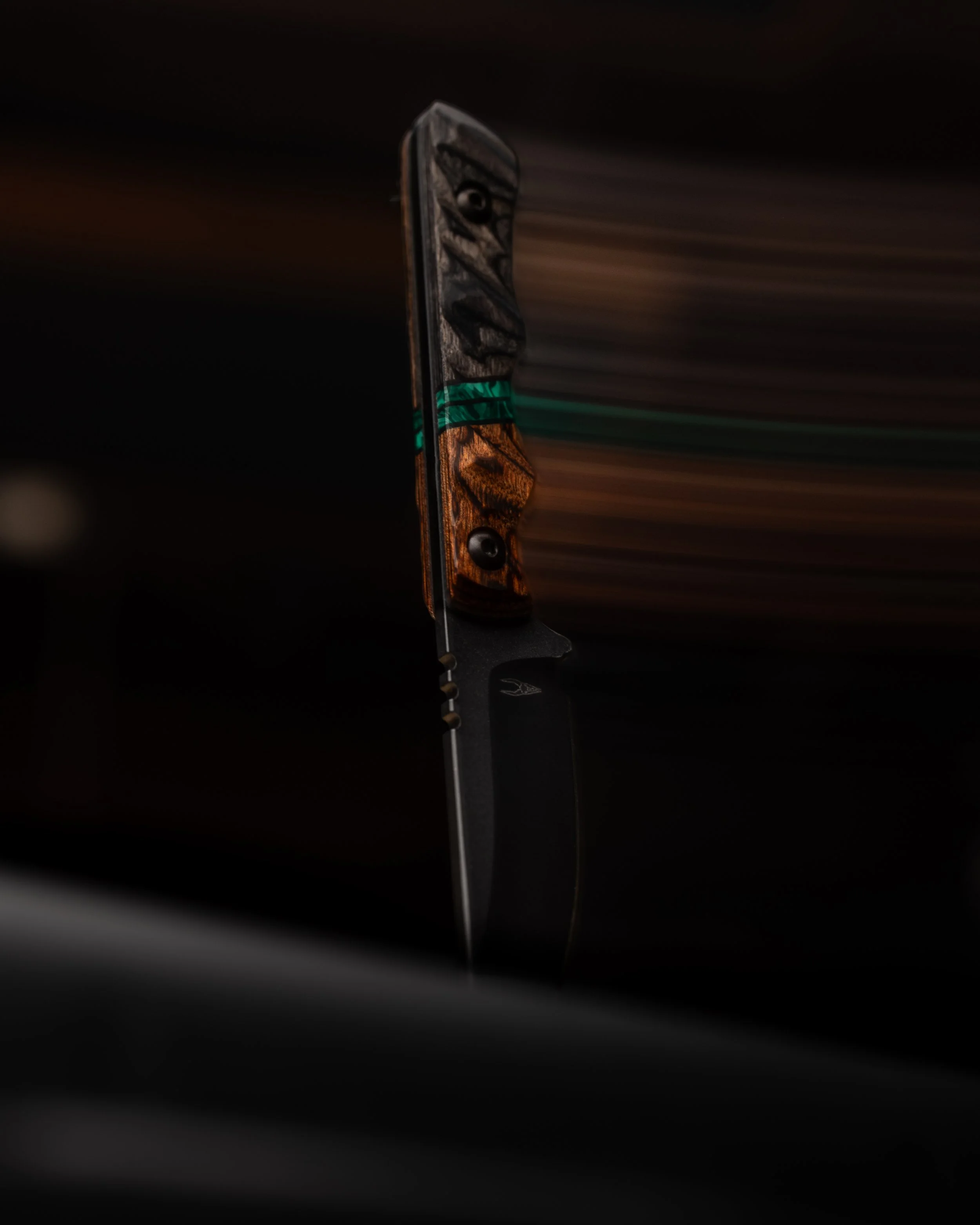 Close-up of a black folding knife with a textured handle, partially open and set against a blurred dark background.