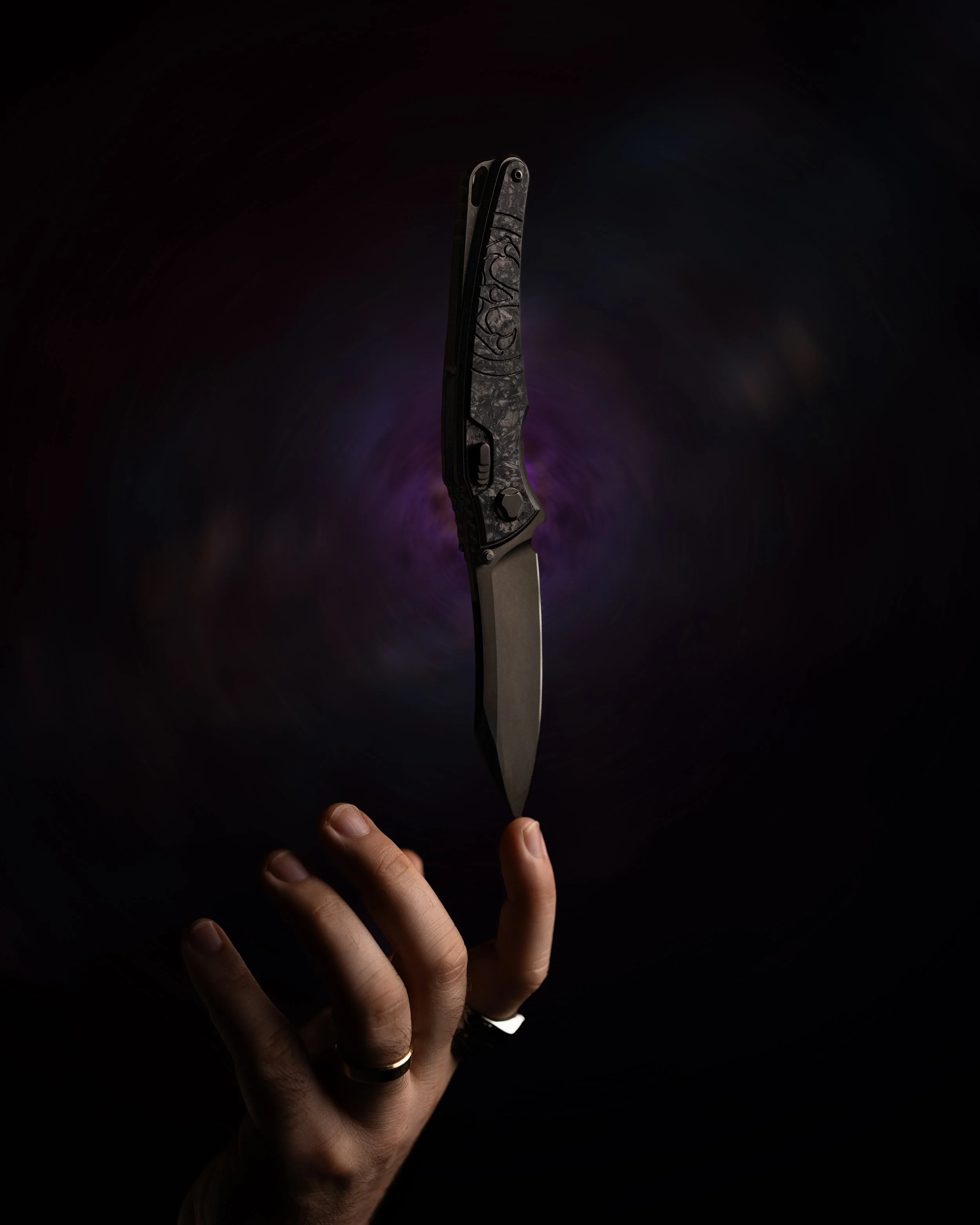 A hand with rings holding a butterfly knife with a marble pattern on the handle against a dark background with a purple glow.