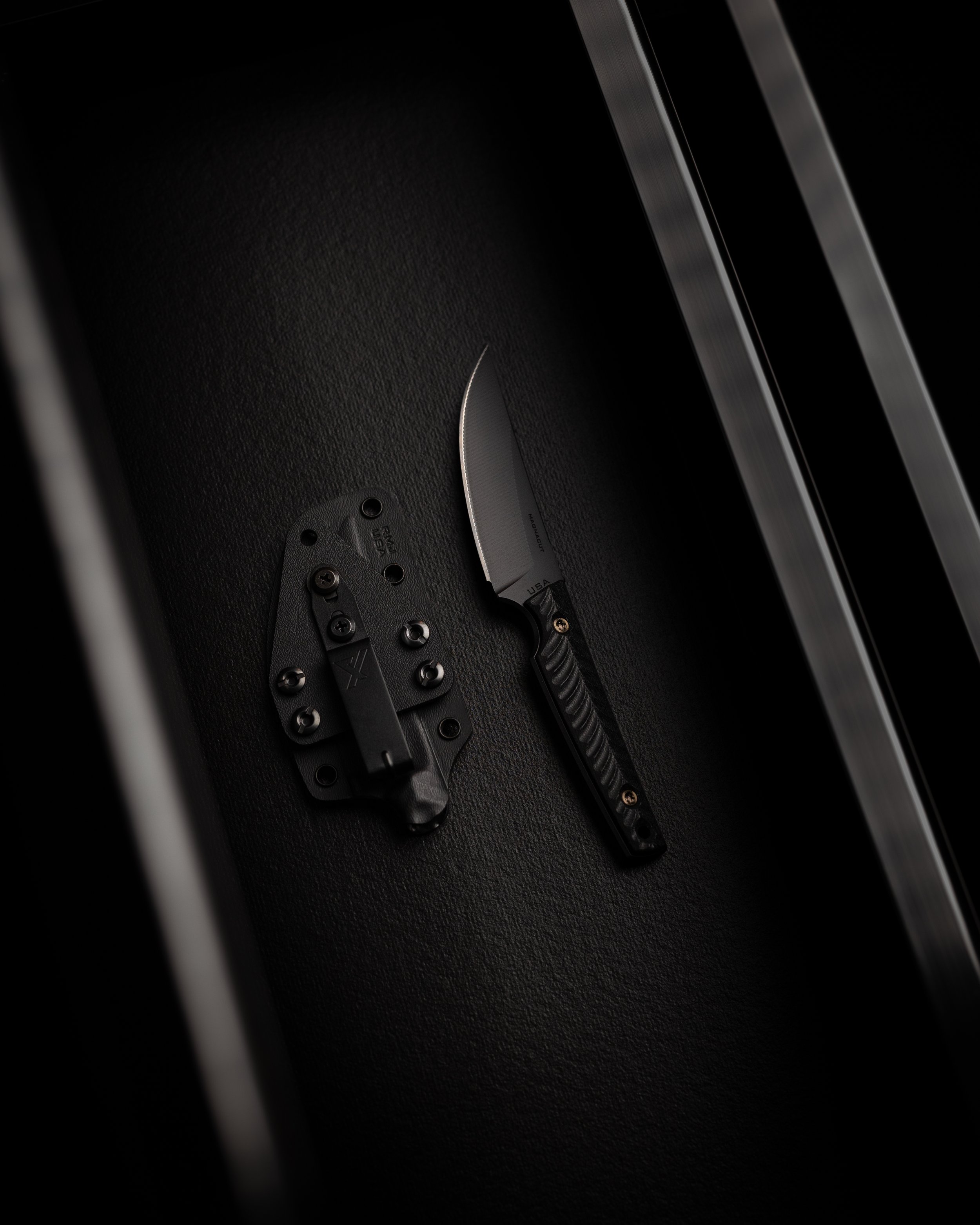 Close-up image of a kitchen knife with a black handle and metal blade, placed on a black textured surface.