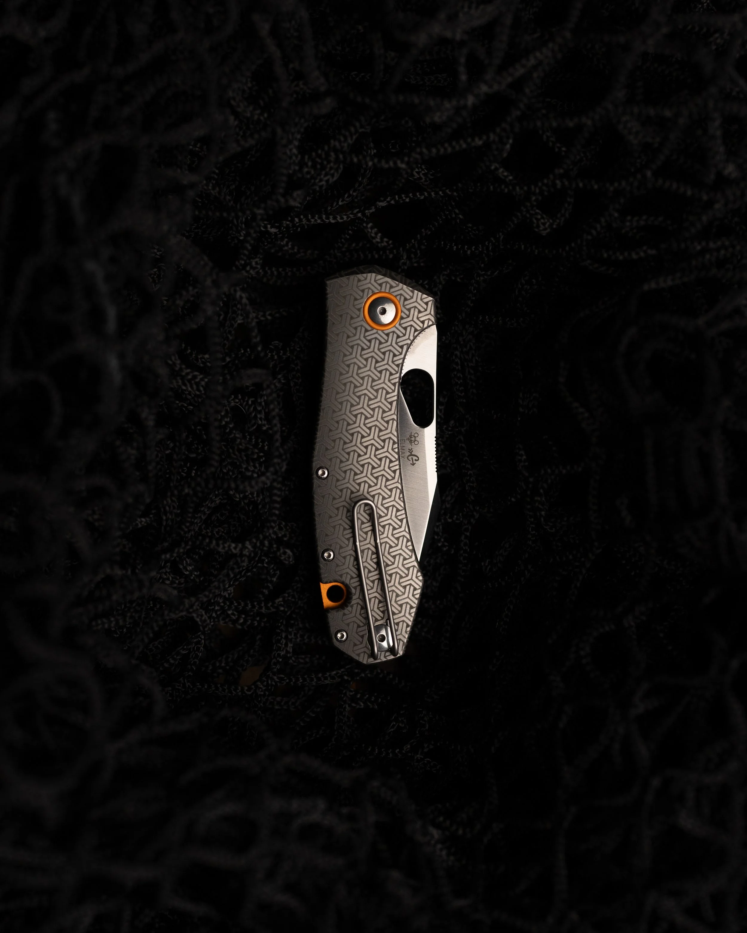 Close-up of a folding pocket knife with a textured handle placed on black fabric with a patterned texture.