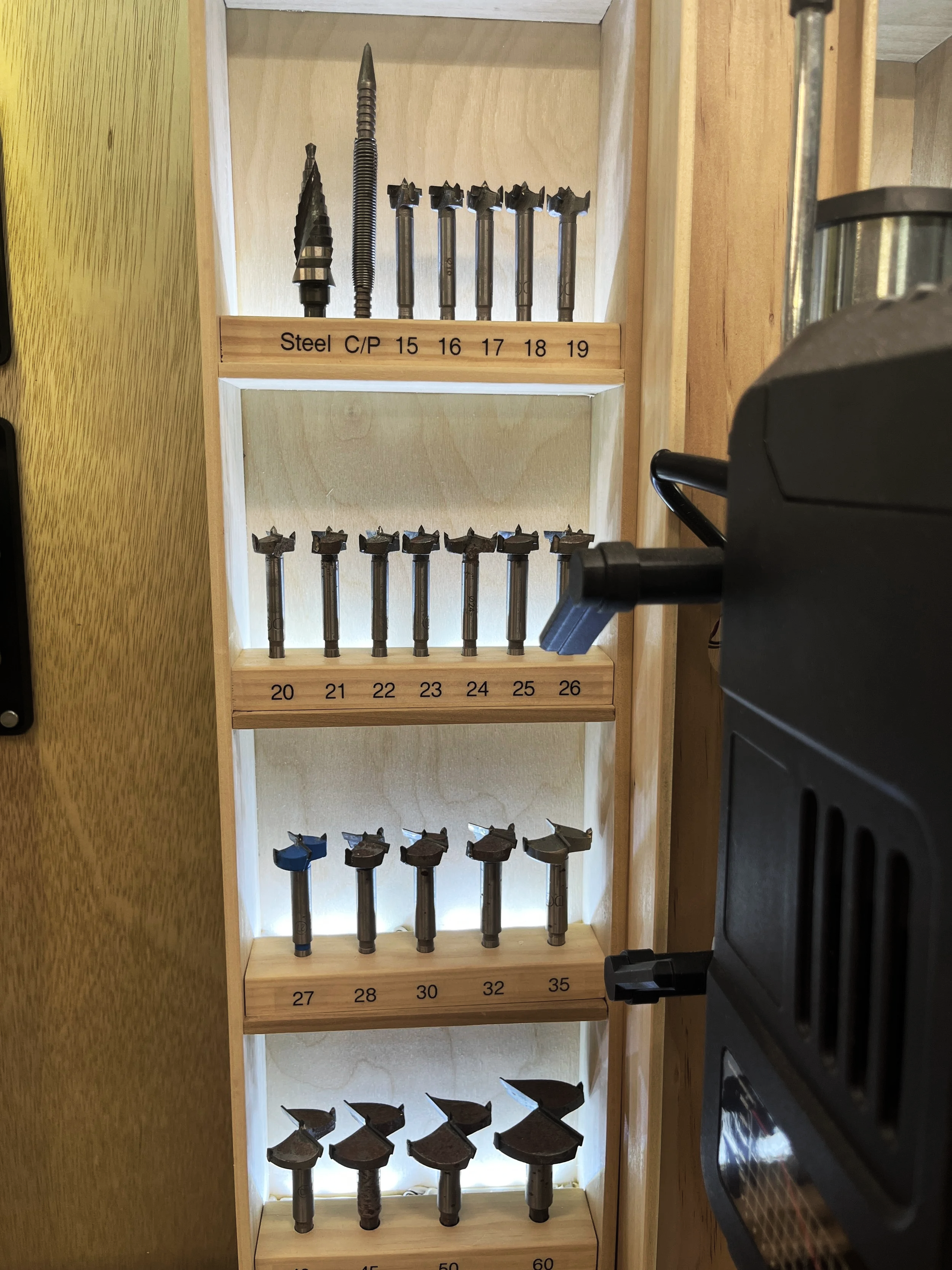 Backlit drill bit storage organized beside the drill press